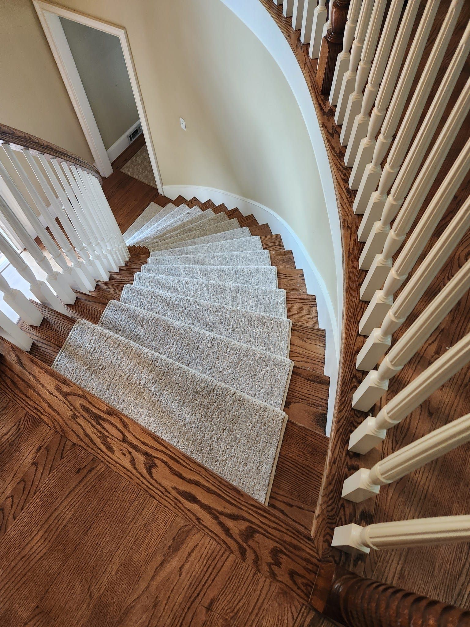 Wooden staircase with carpet runner, white railing, curved design.