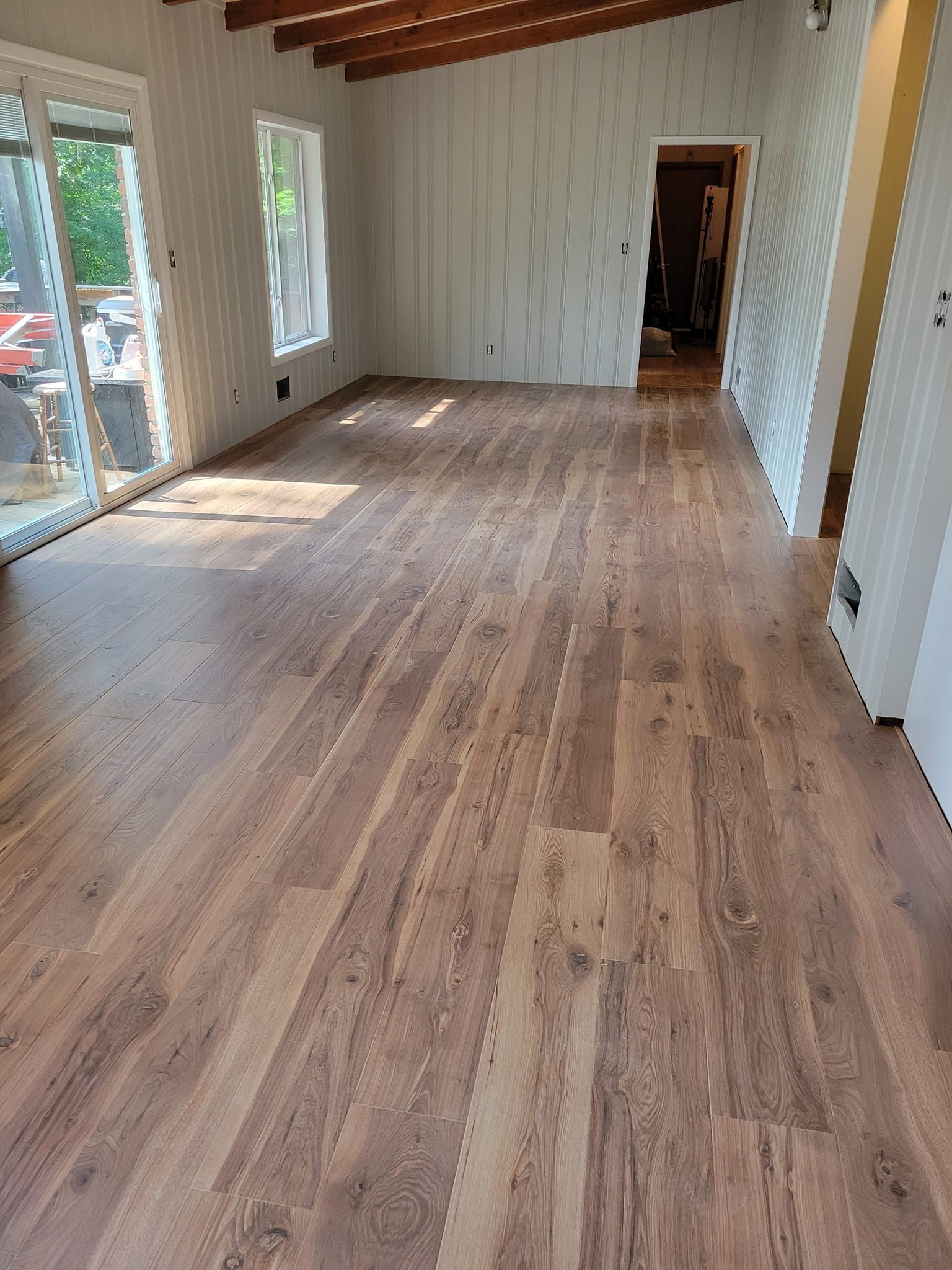 Empty room with wood-look flooring, white walls, and a door, natural light from a window and door.
