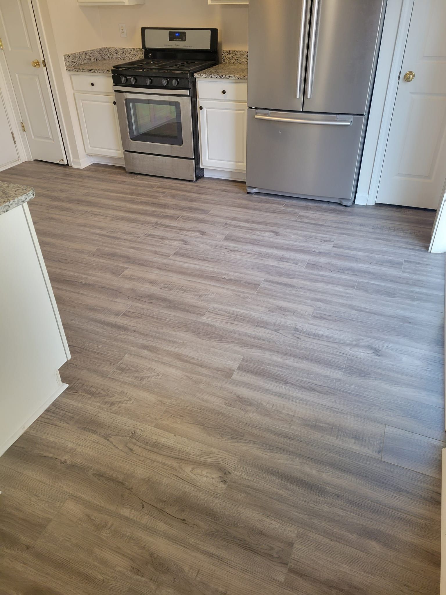Kitchen with gray wood-look flooring, white cabinets, stainless steel appliances, and granite countertops.