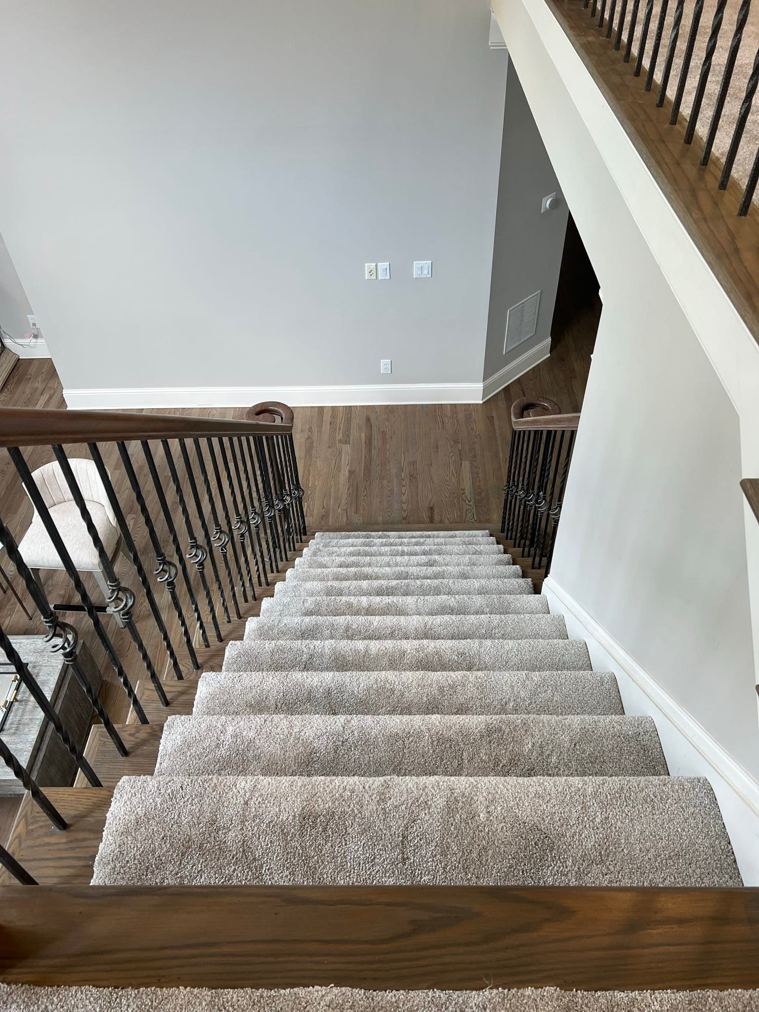 Downward view of carpeted stairs with a dark wood railing and black iron balusters.