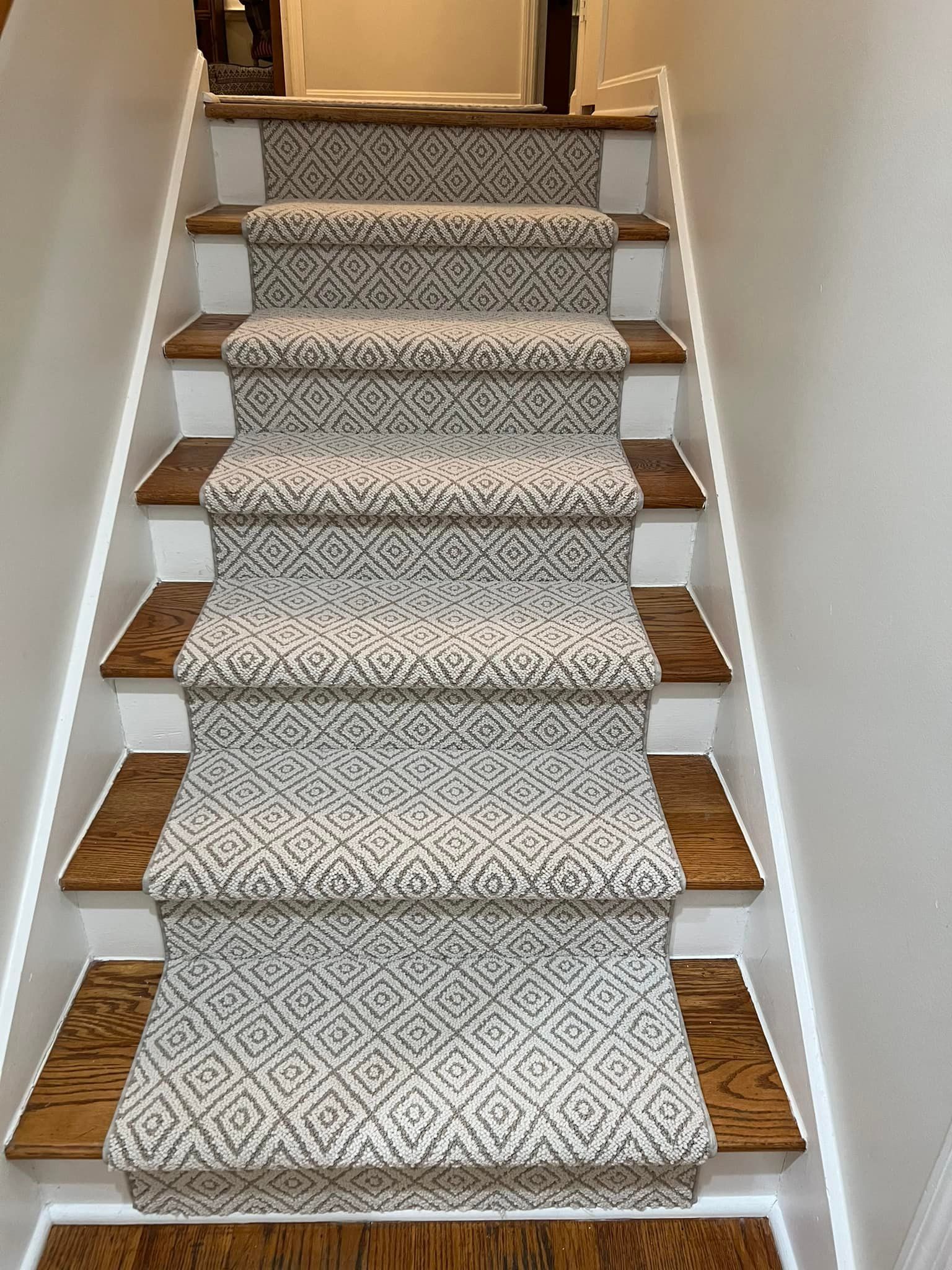 Staircase with patterned gray and white carpet runner, brown wood treads, and white risers.