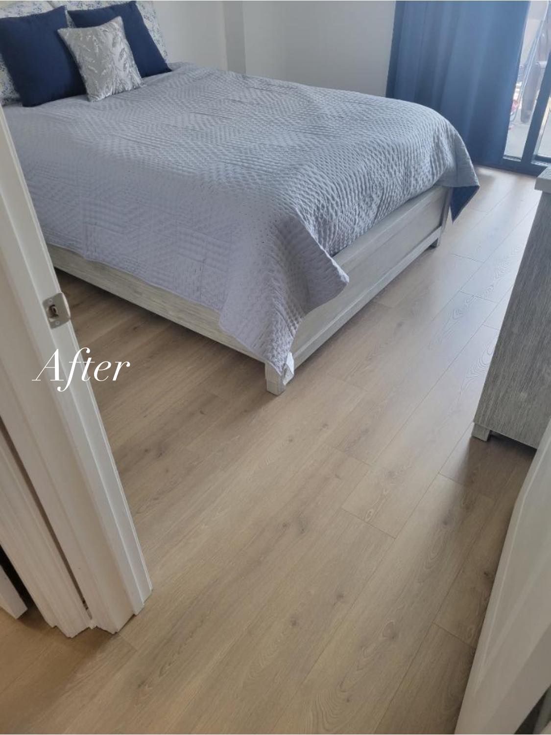 Bedroom with a light-colored wood floor, bed with blue bedding and pillows, next to a window.
