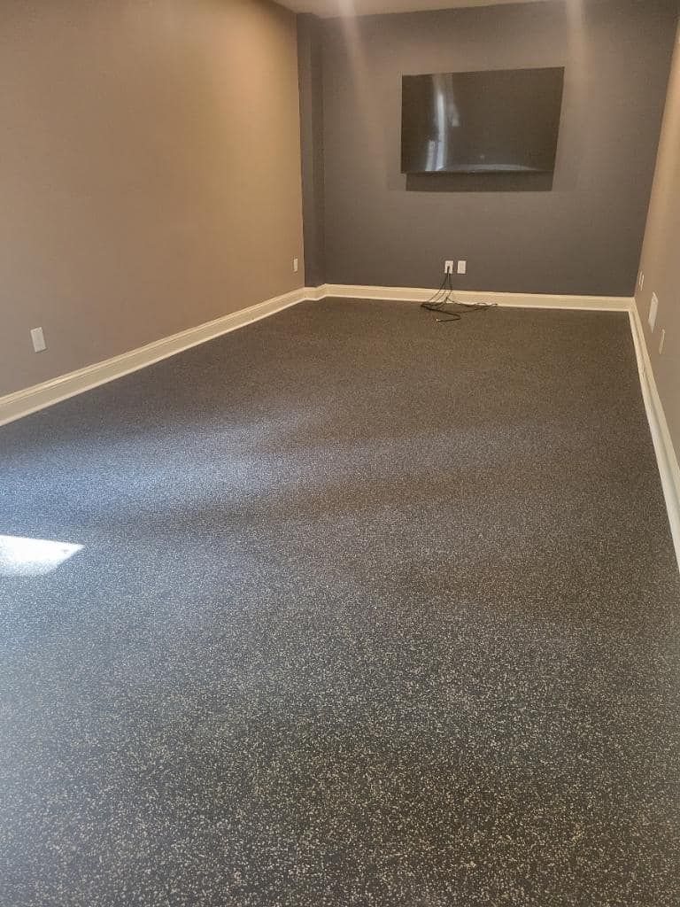 Empty room with dark speckled flooring, gray walls, and a mounted TV.