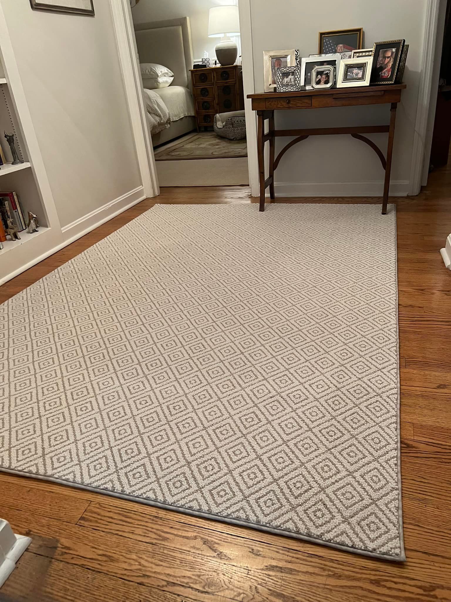 A rectangular patterned rug on a hardwood floor, next to a small wooden table with framed photos.