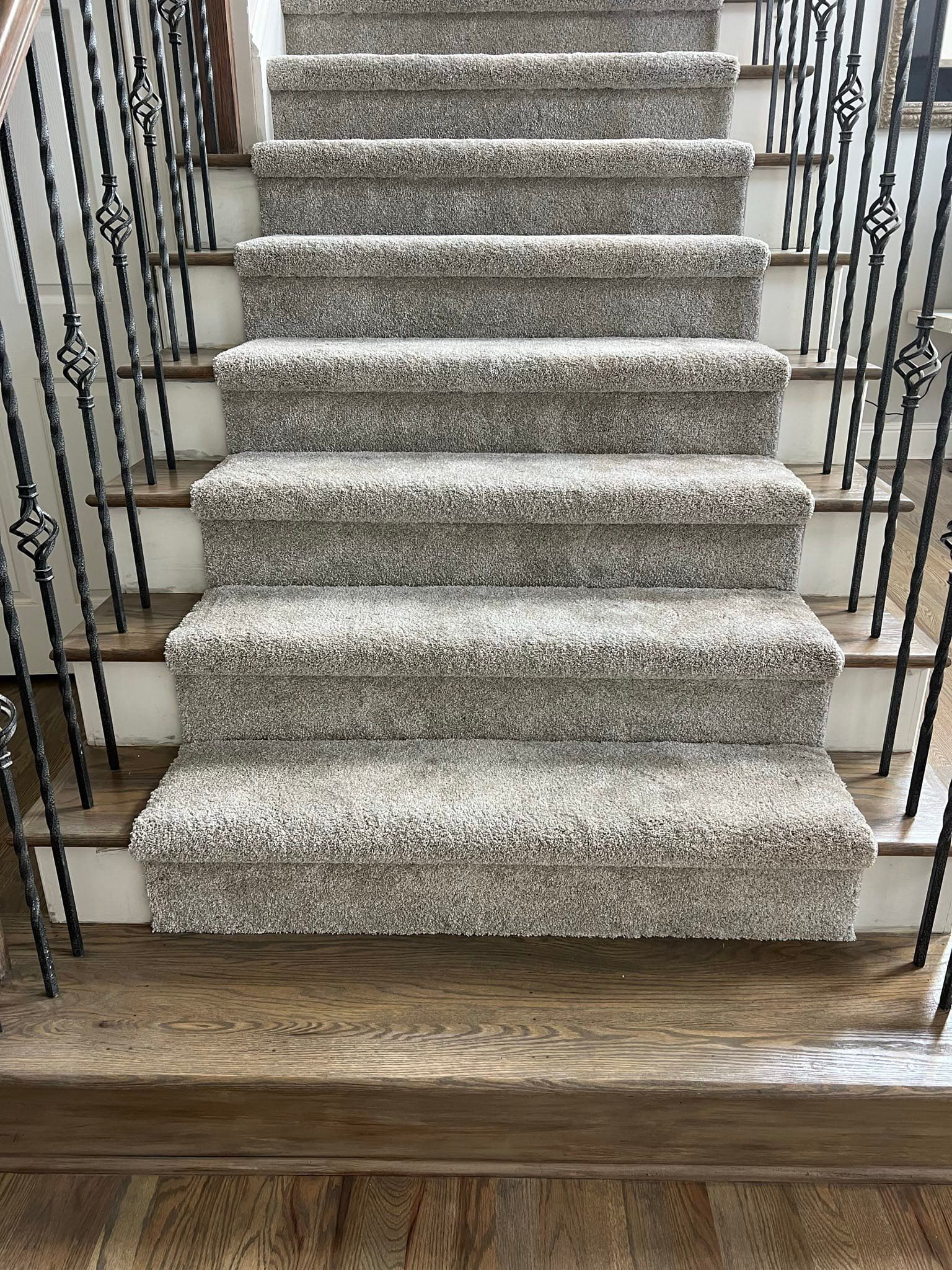 Carpeted staircase with dark metal railing. Light brown carpet on wooden steps.