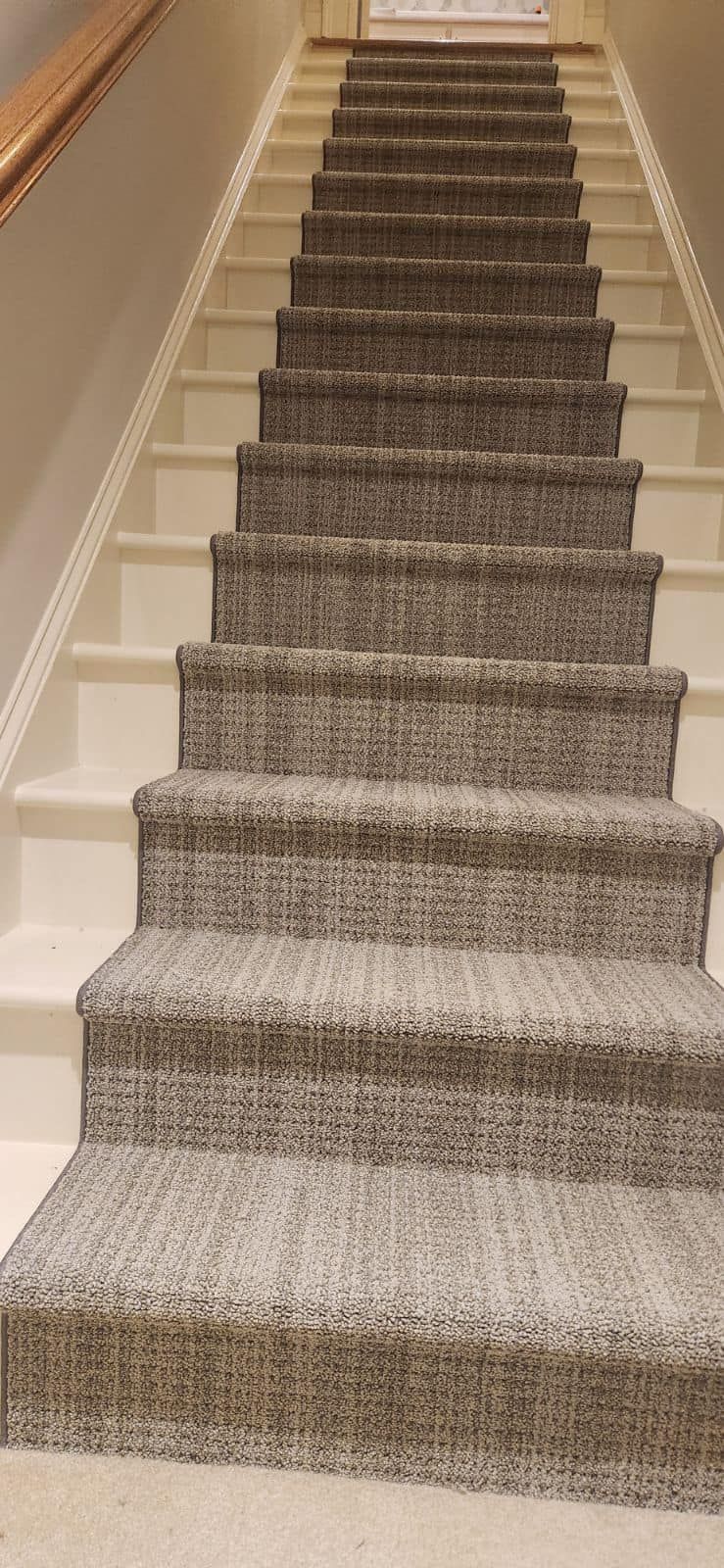 Staircase with gray carpeted steps and white painted risers. Wooden handrail on the left.