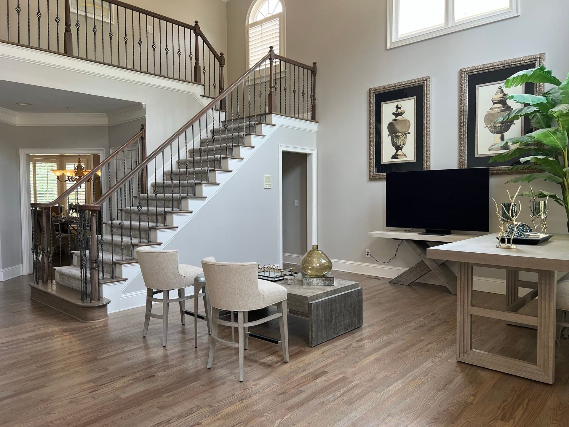 A grand foyer with a staircase, hardwood floors, neutral walls, and a large TV.
