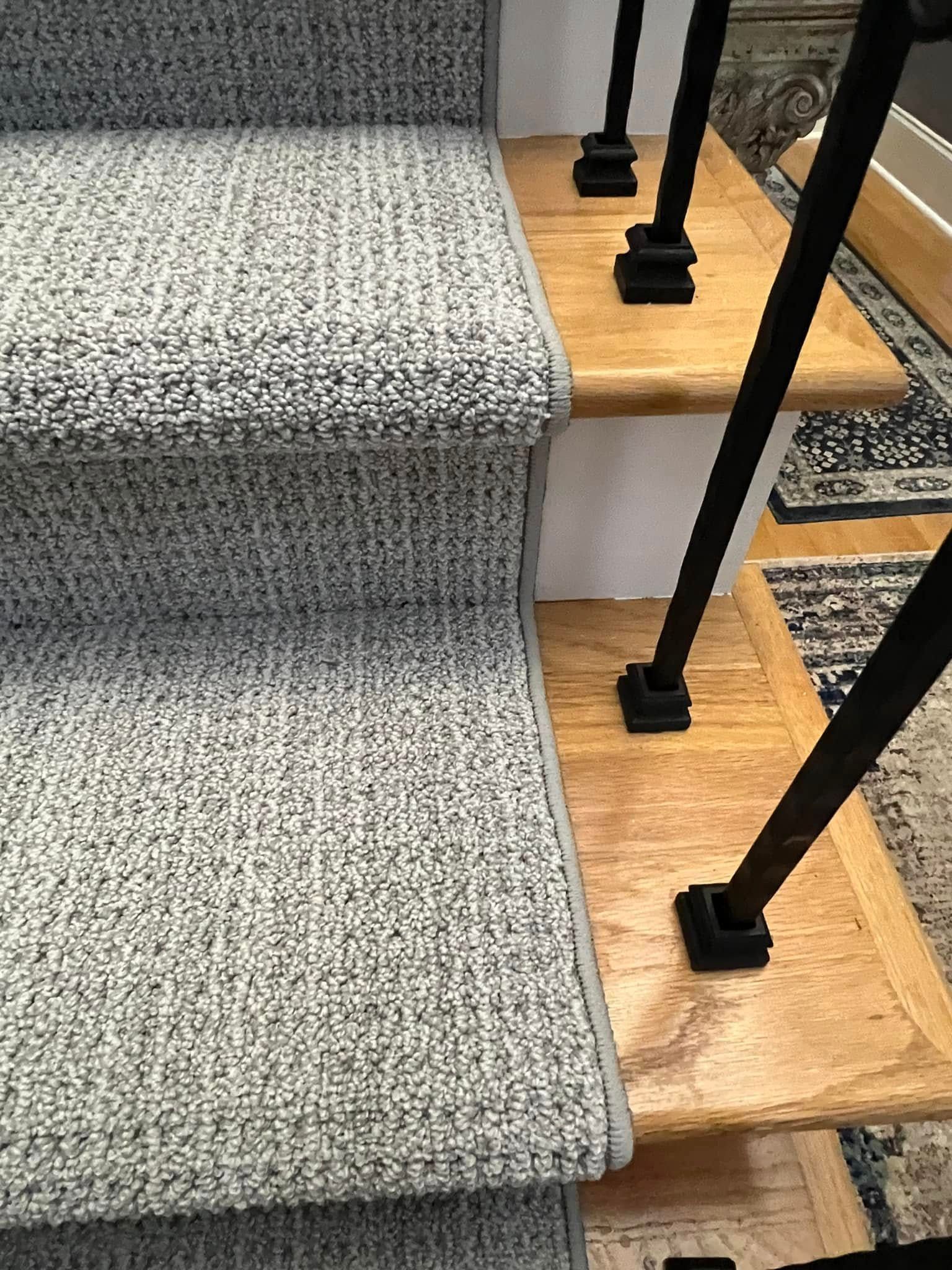 Carpeted gray stairs with wooden treads and black railing.
