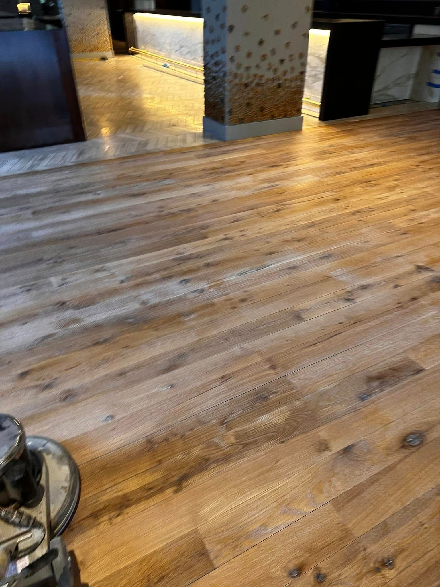 Wooden floor being refinished with a floor buffer in a commercial setting.