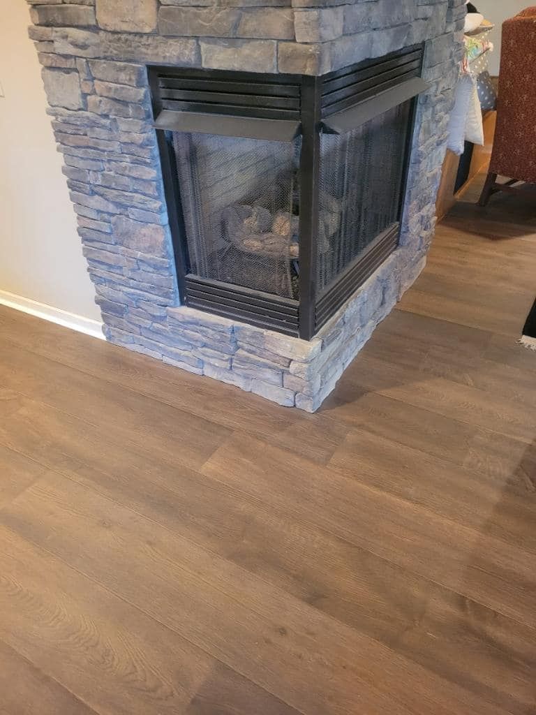 Corner fireplace with gray stone surround, black metal screen, and brown wood-look flooring.