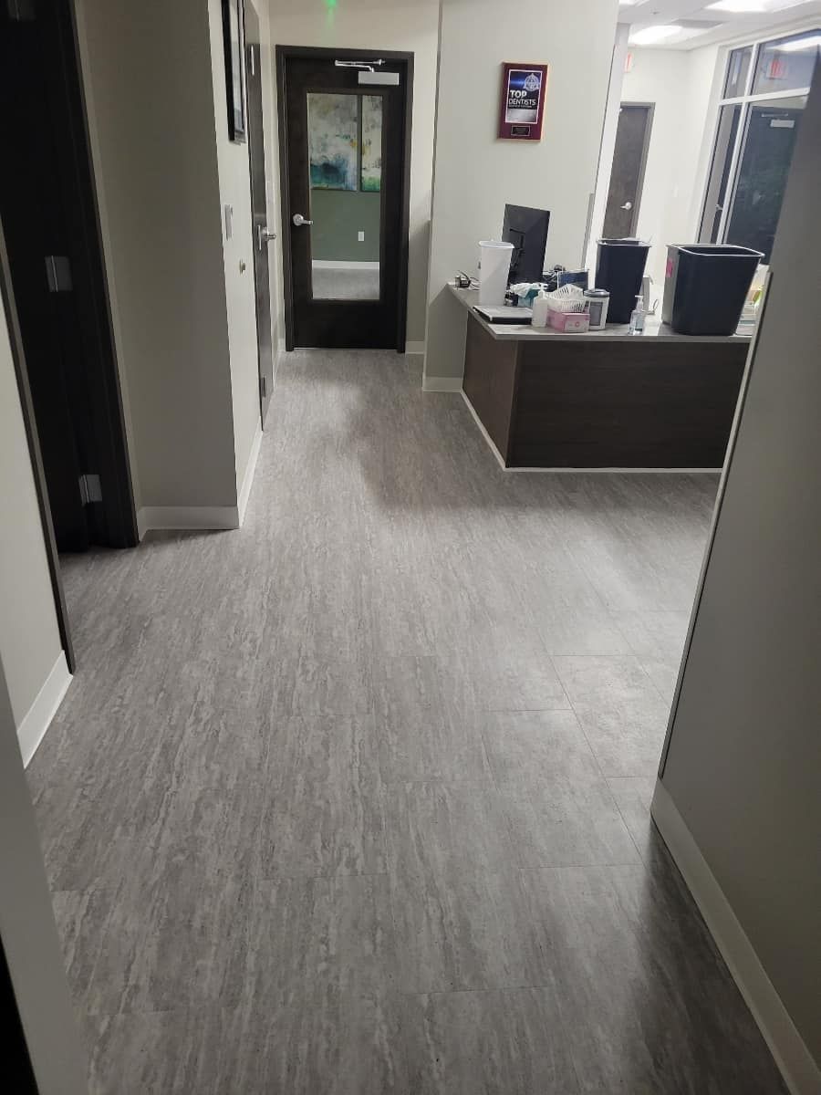 Hallway with gray wood-look flooring, leading to a front desk and a door with a glass panel.