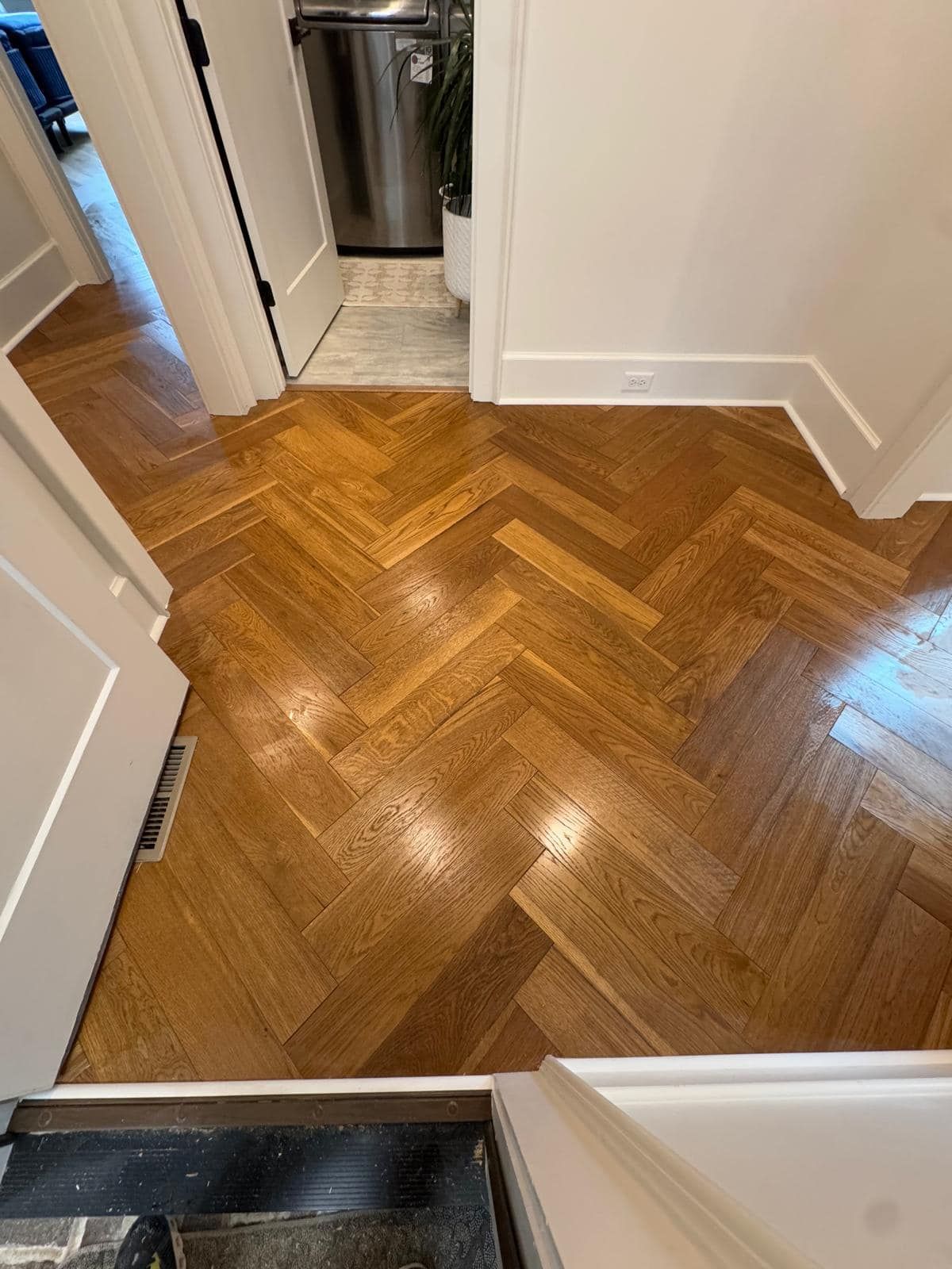 Herringbone pattern hardwood floor in hallway with white trim and doorways.