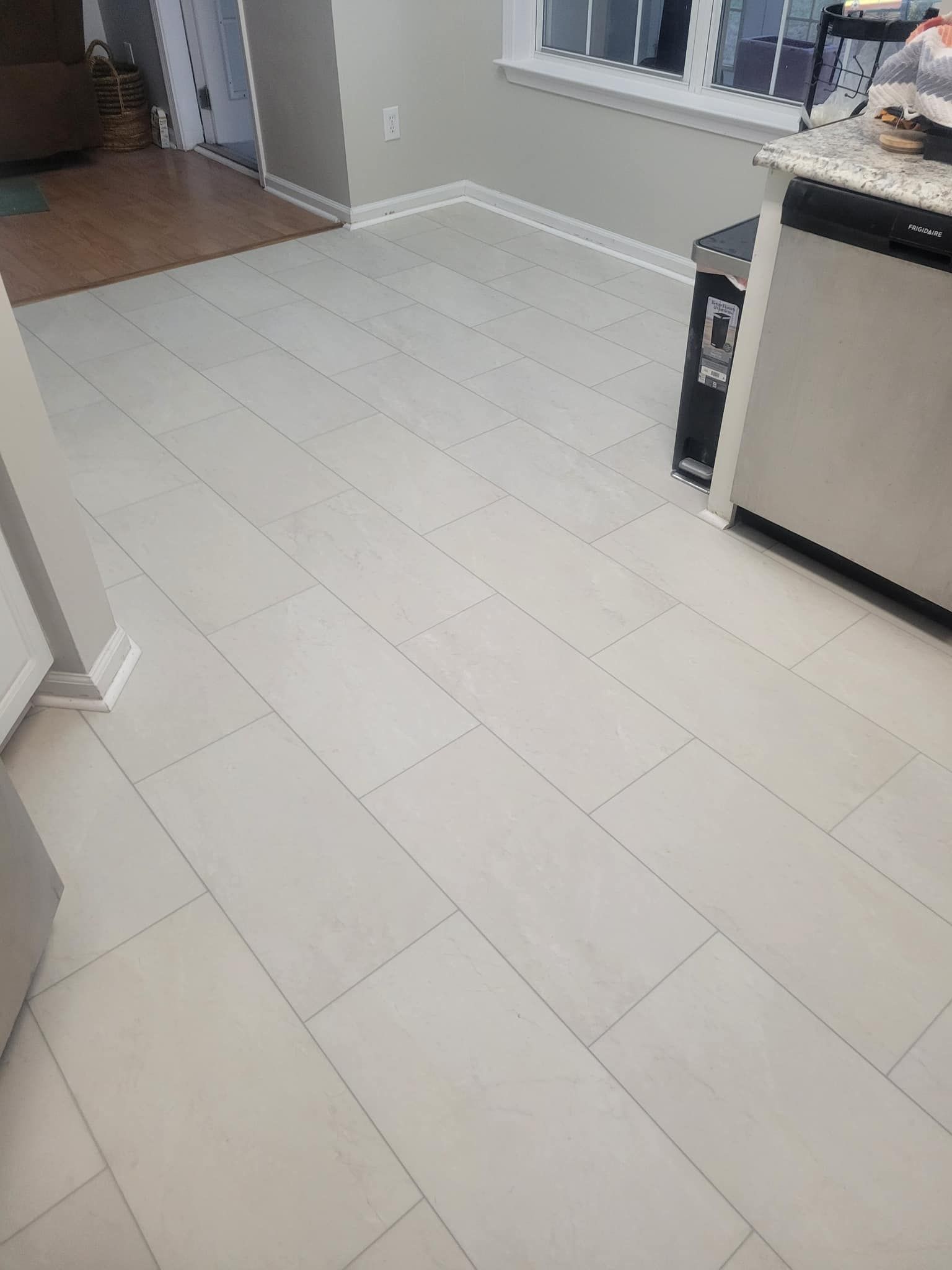 Light-colored wood-look flooring in a kitchen. A white appliance is visible, along with a window.