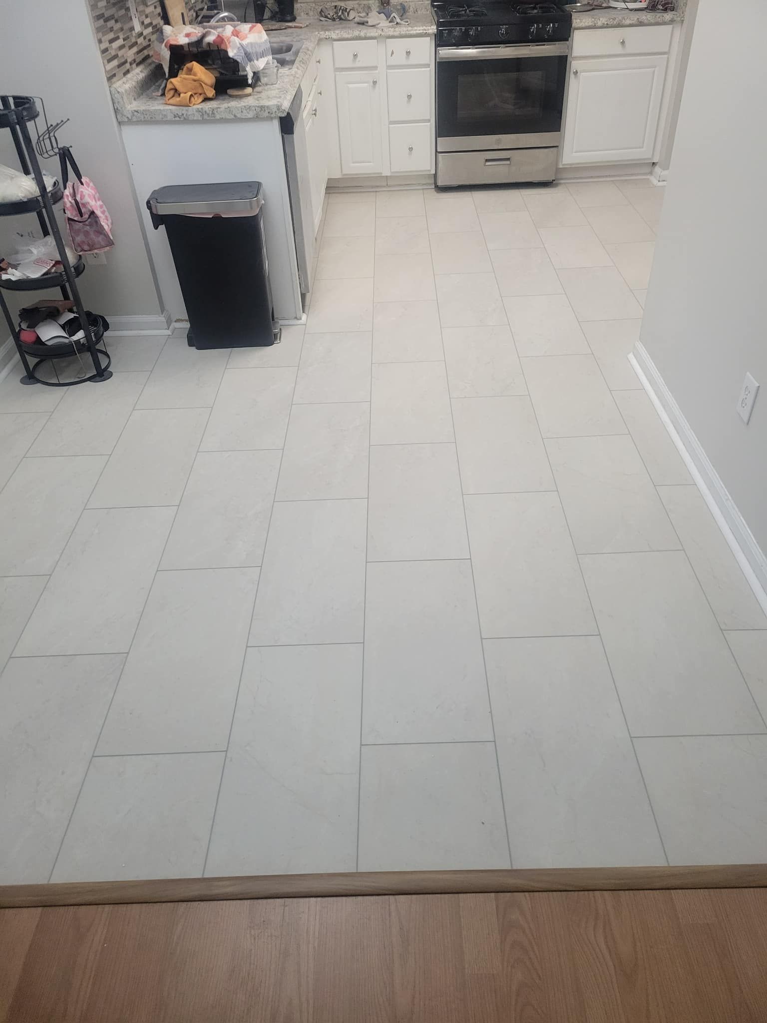 Kitchen with white tiled floor, white cabinets, and stainless steel appliances. A black trash can is next to the cabinets.