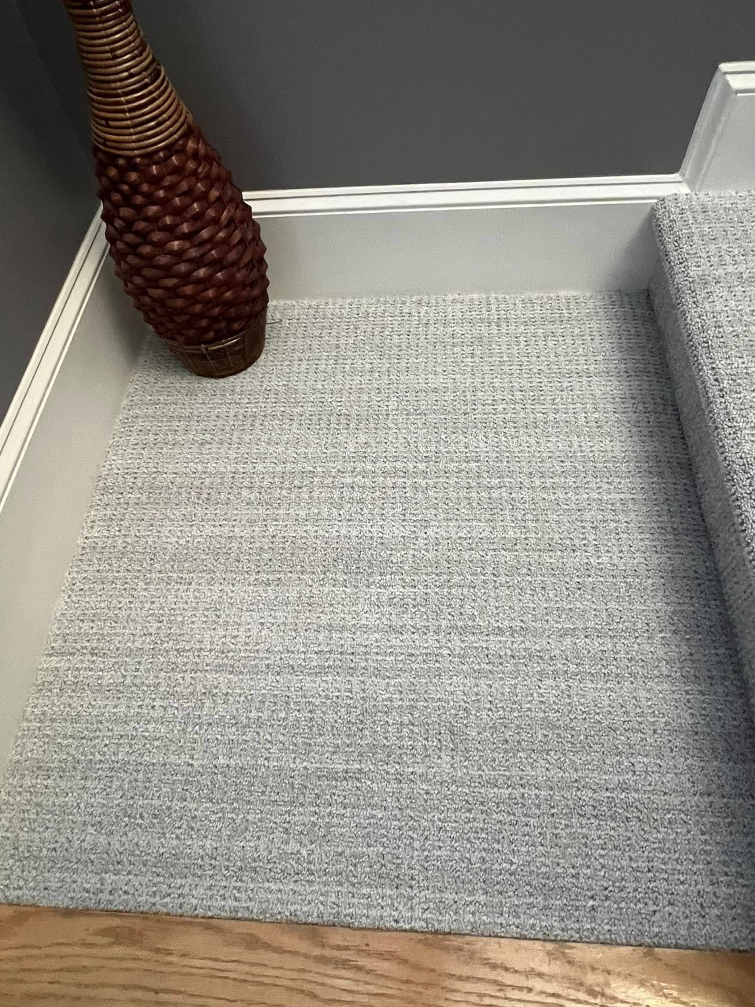 Staircase with gray carpet runner and decorative woven vase in corner, near gray wall and wooden floor.