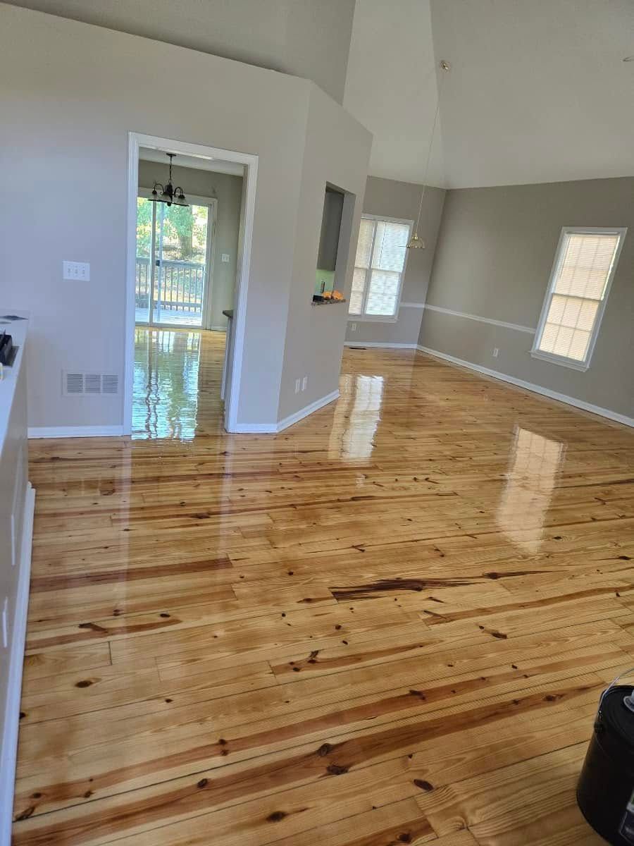 Wooden floors in a room, reflecting light. Gray walls, two windows, and a doorway to another room.