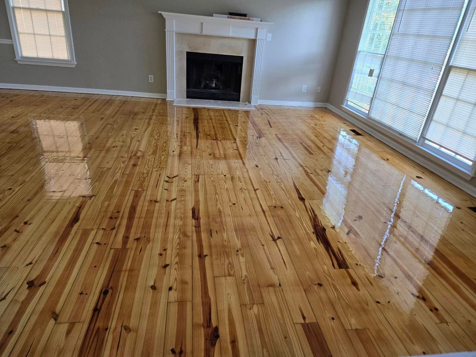 Wooden floor reflecting natural light in a living room with a fireplace and large windows.
