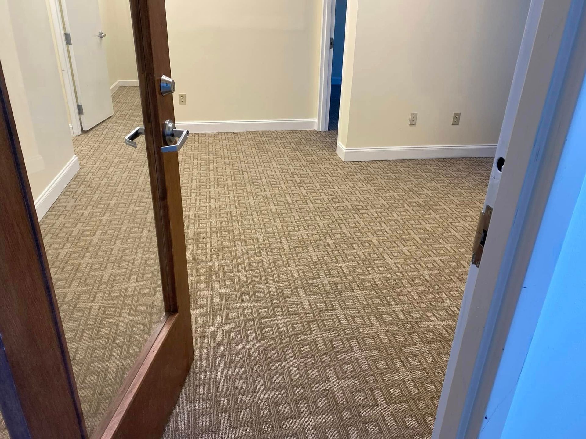 Open door into a beige carpeted room with white trim and a hallway visible.