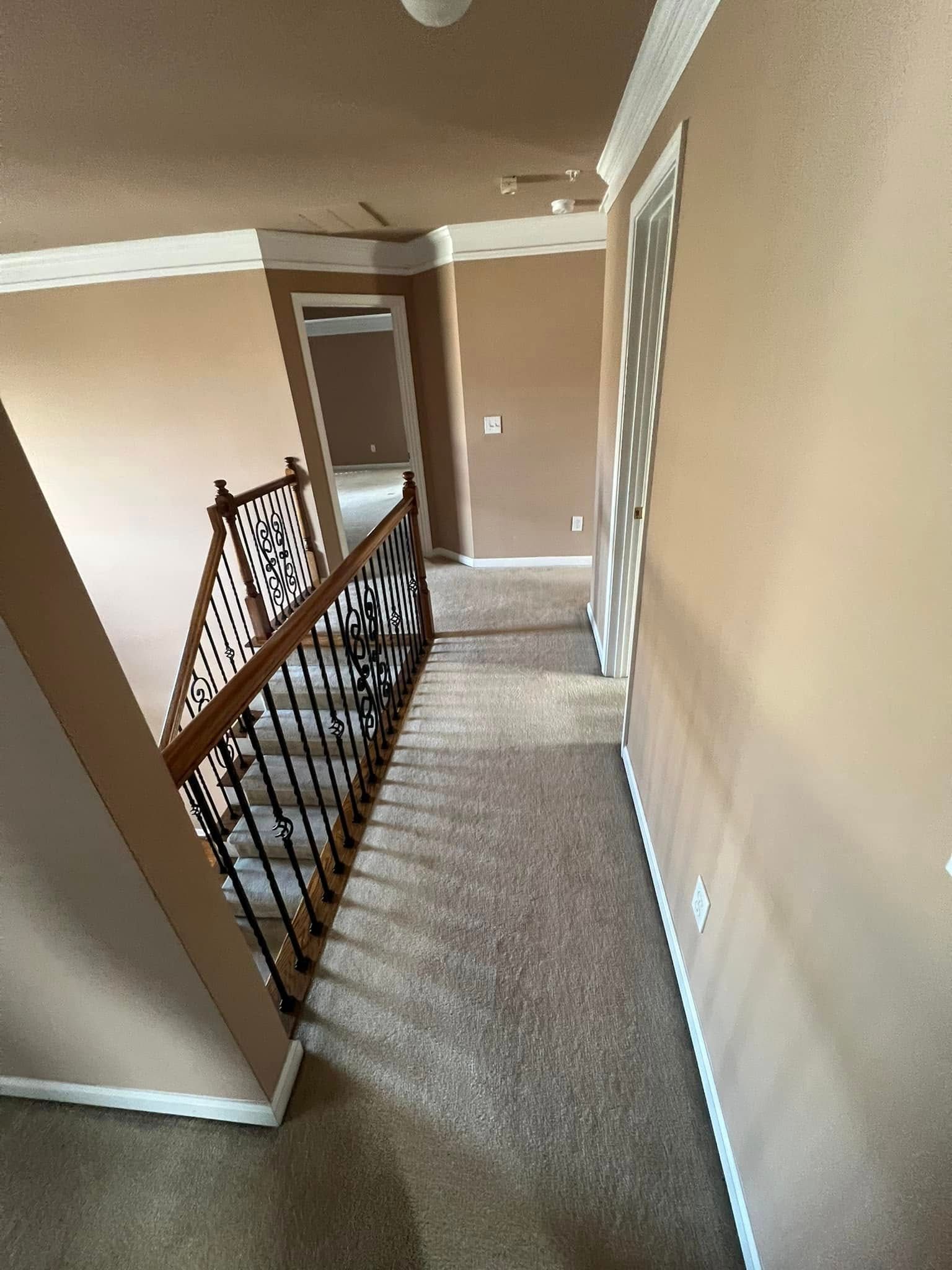 Hallway with carpet and staircase, tan walls, door on right, door at end, and light fixtures.