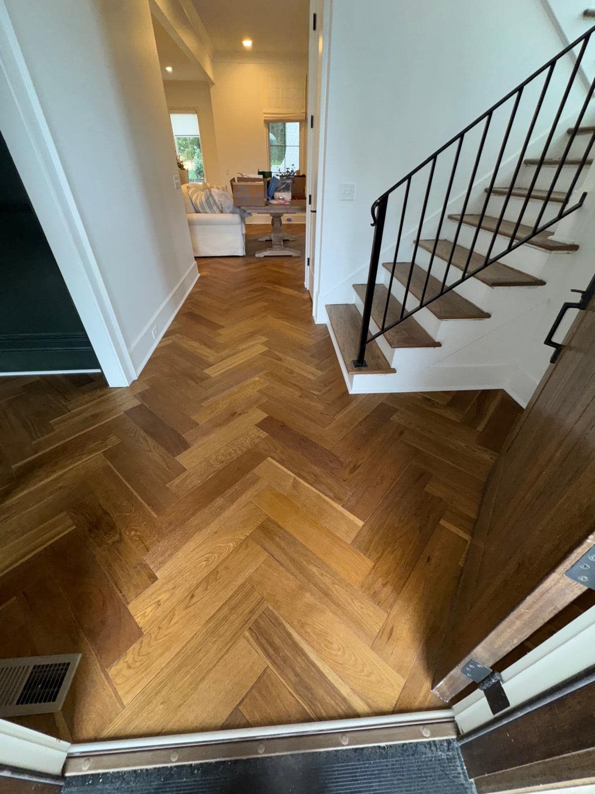 Herringbone wood floor in a house entryway, leading to stairs. Dark brown, white trim.