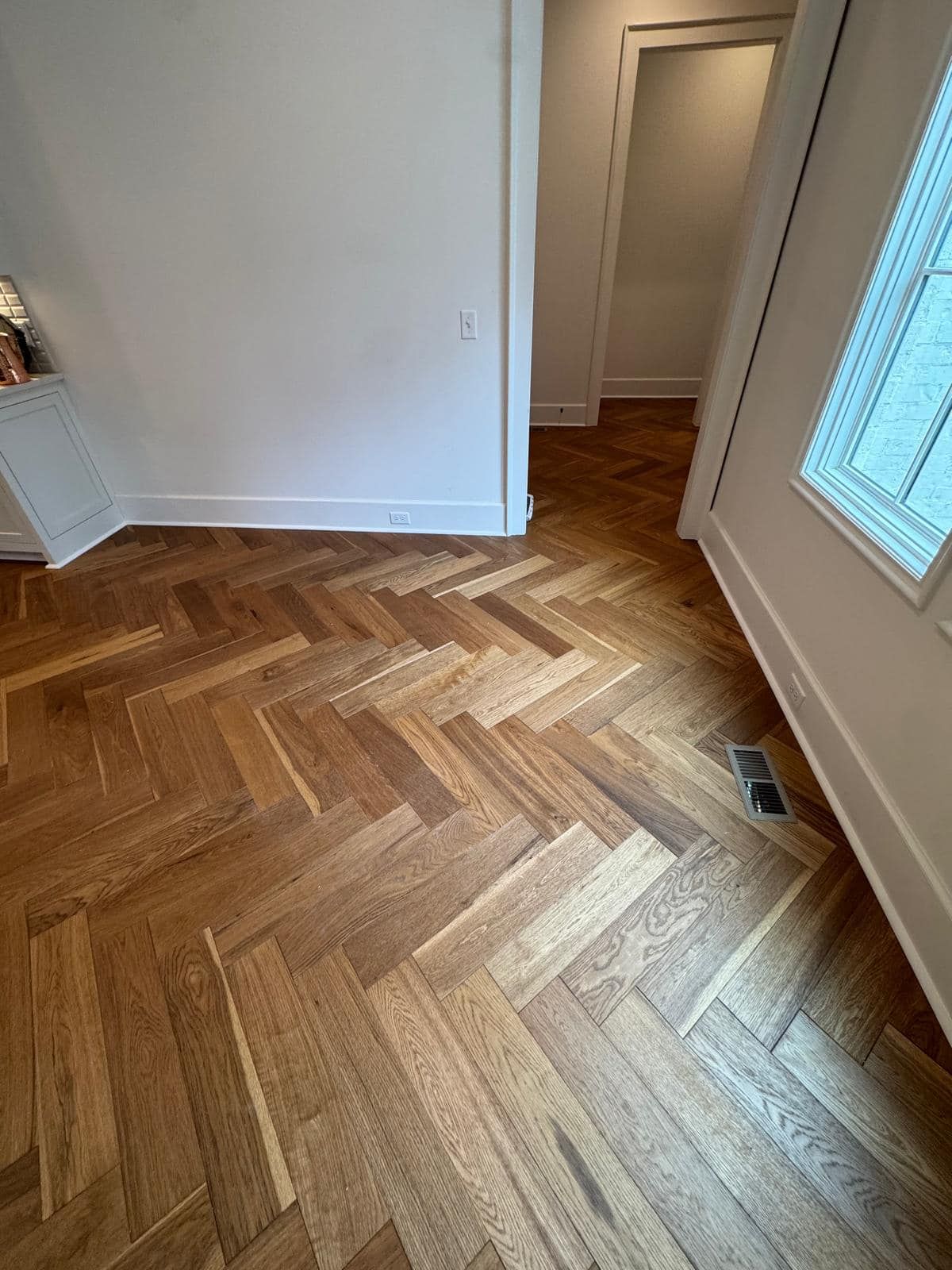 Herringbone wood floor, white walls, and a doorway.