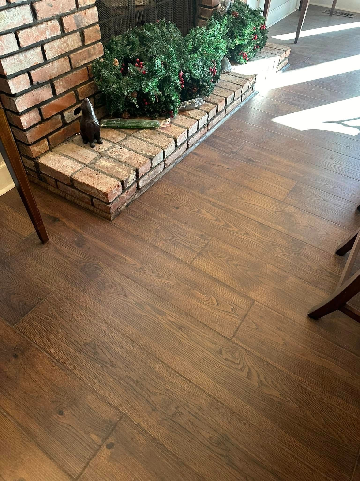 Wooden floor in front of a brick fireplace with greenery.