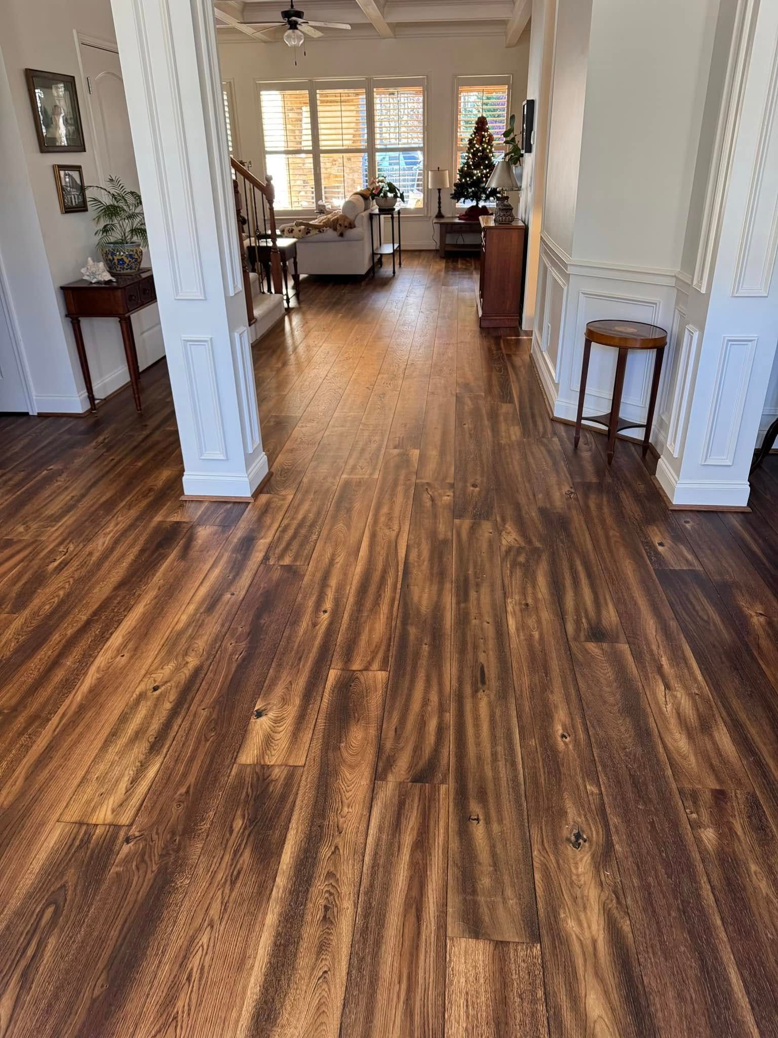 Hardwood floor in a home's entryway. Dark brown planks with visible grain. White columns and wainscoting frame the space.