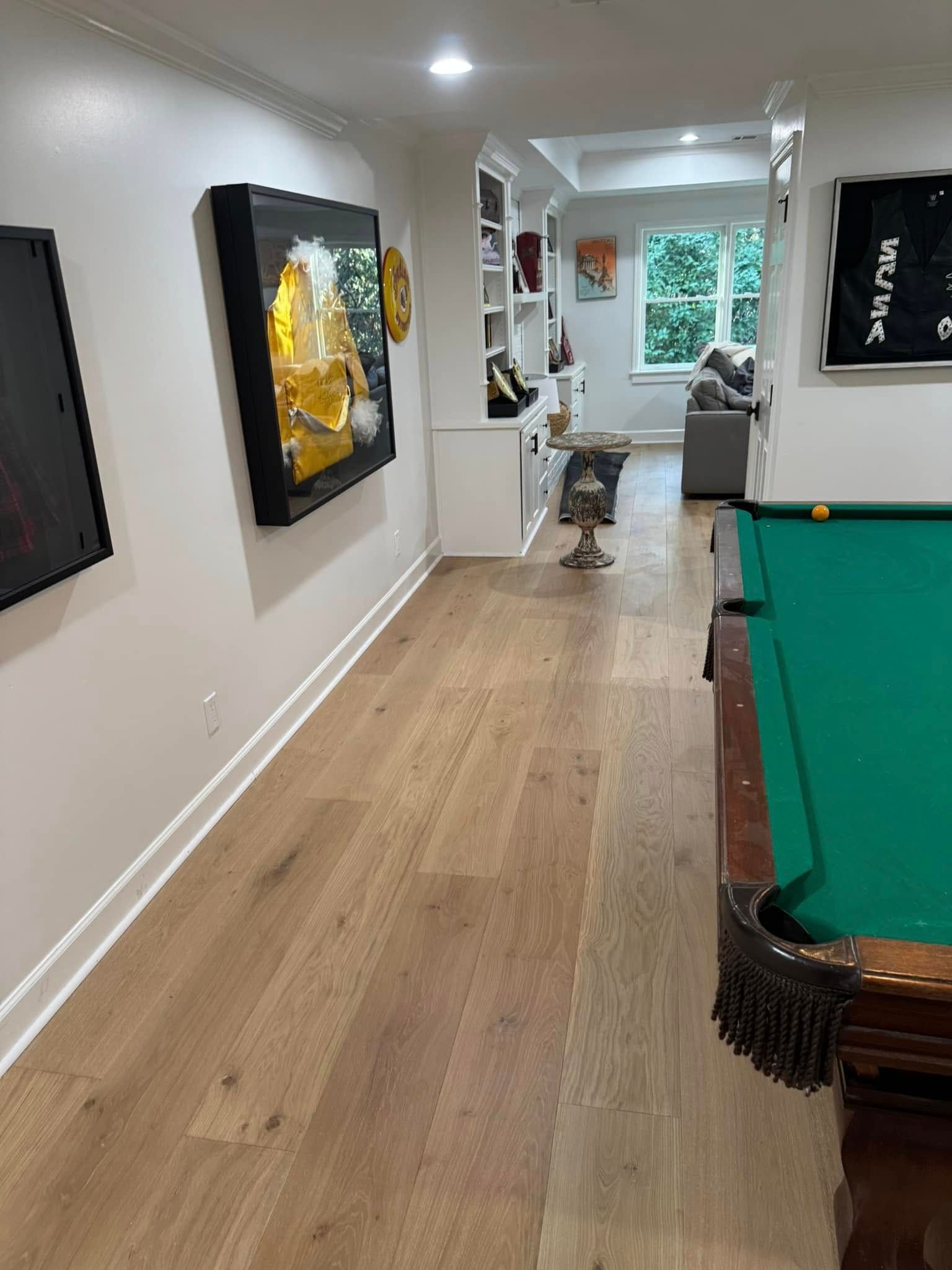Wooden floor leads to a room with a pool table on the right and art on the left.