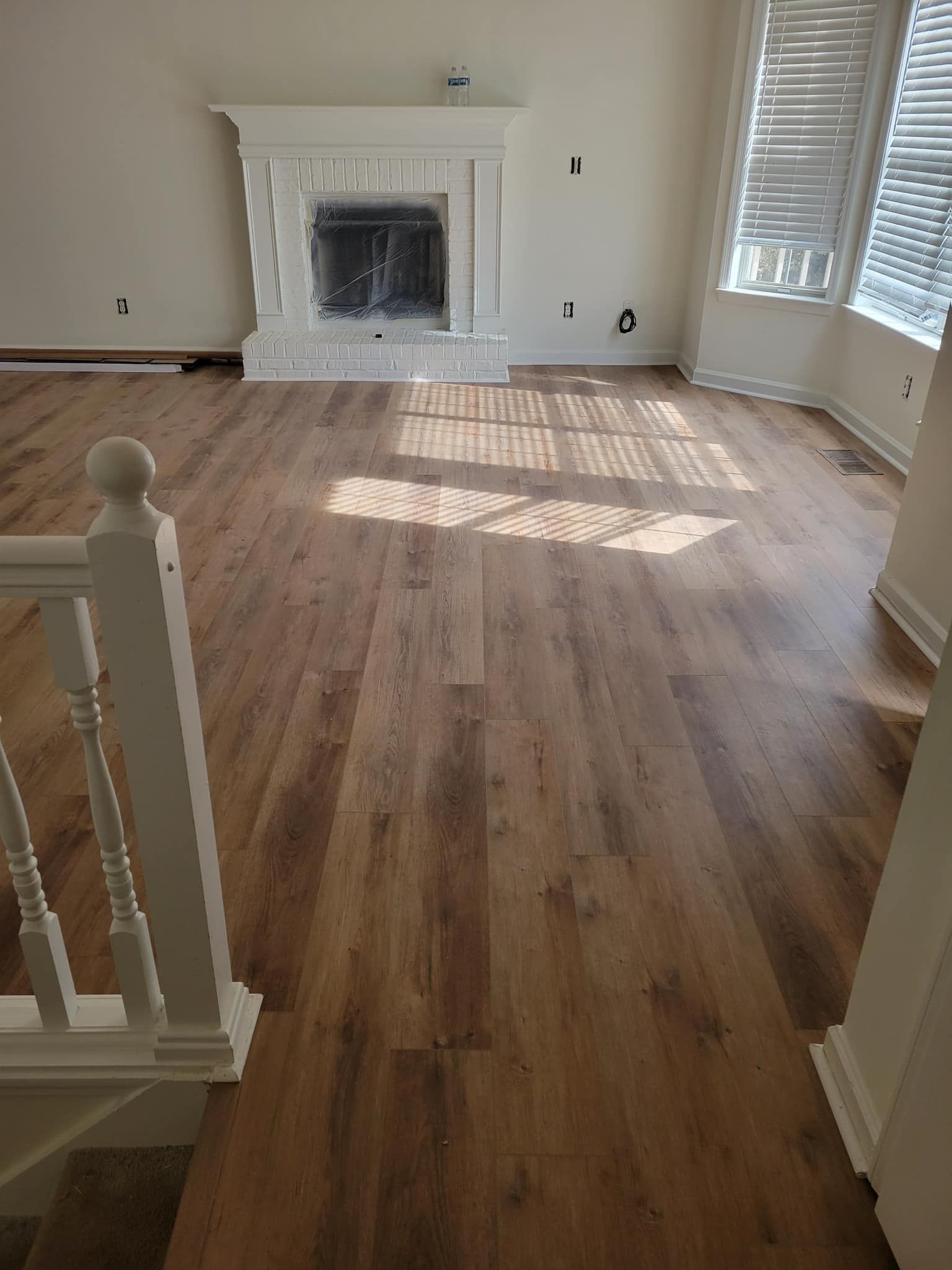 Living room with new wood-look flooring, fireplace, and window with blinds.