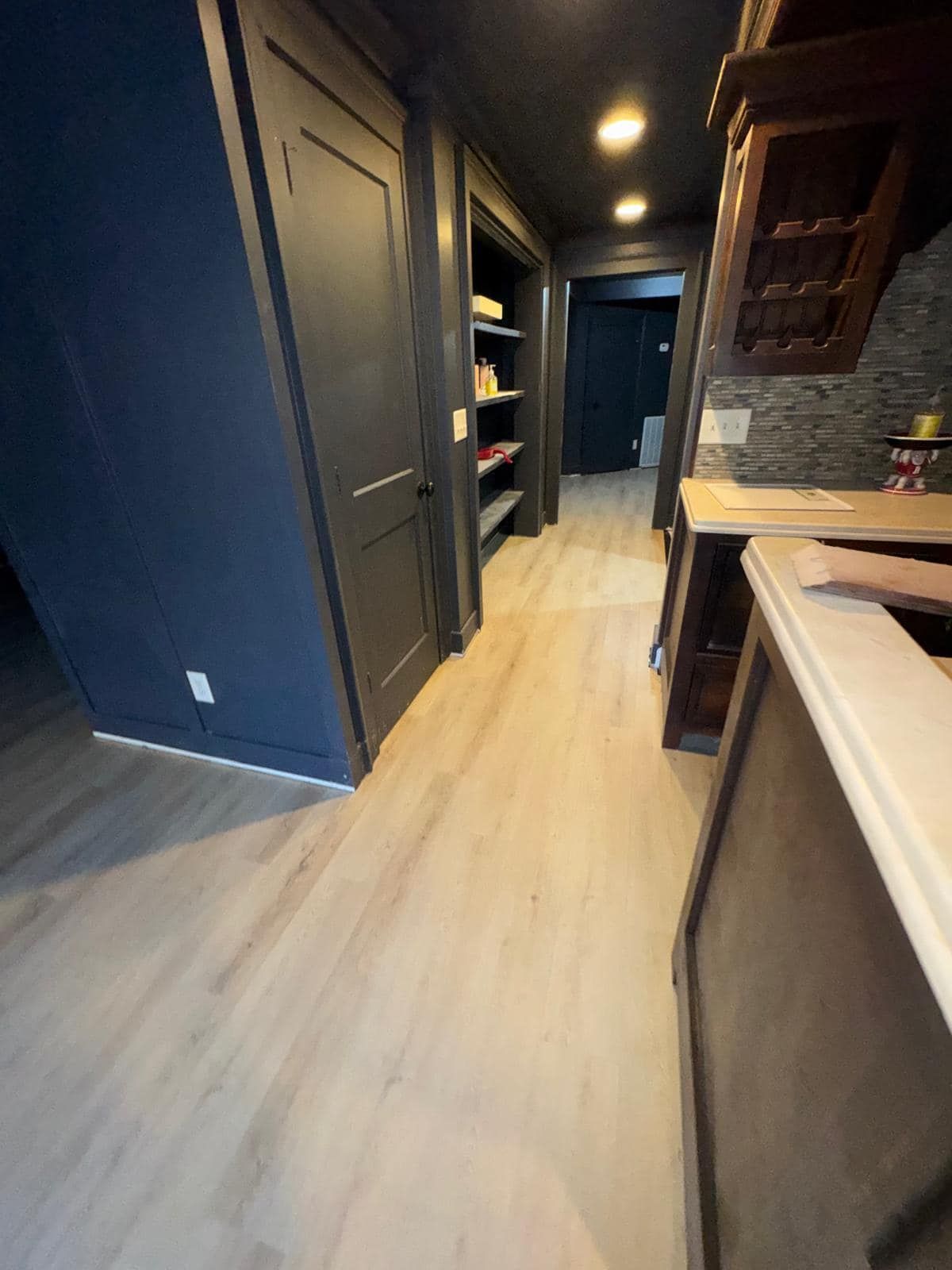 Hallway with light wood floors, dark blue walls, dark cabinets and recessed lights.