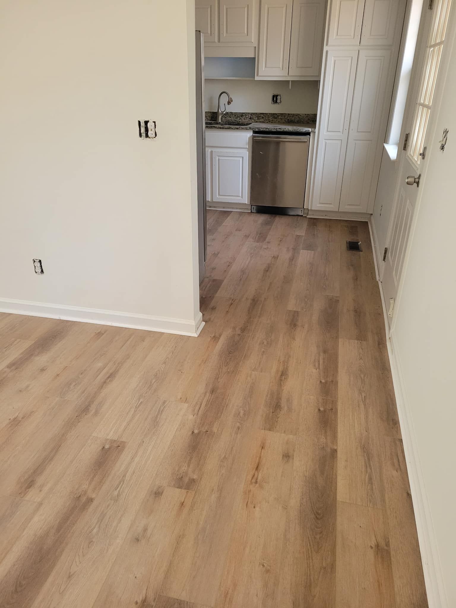 View of newly installed wood-look flooring and a kitchen with stainless steel appliances.