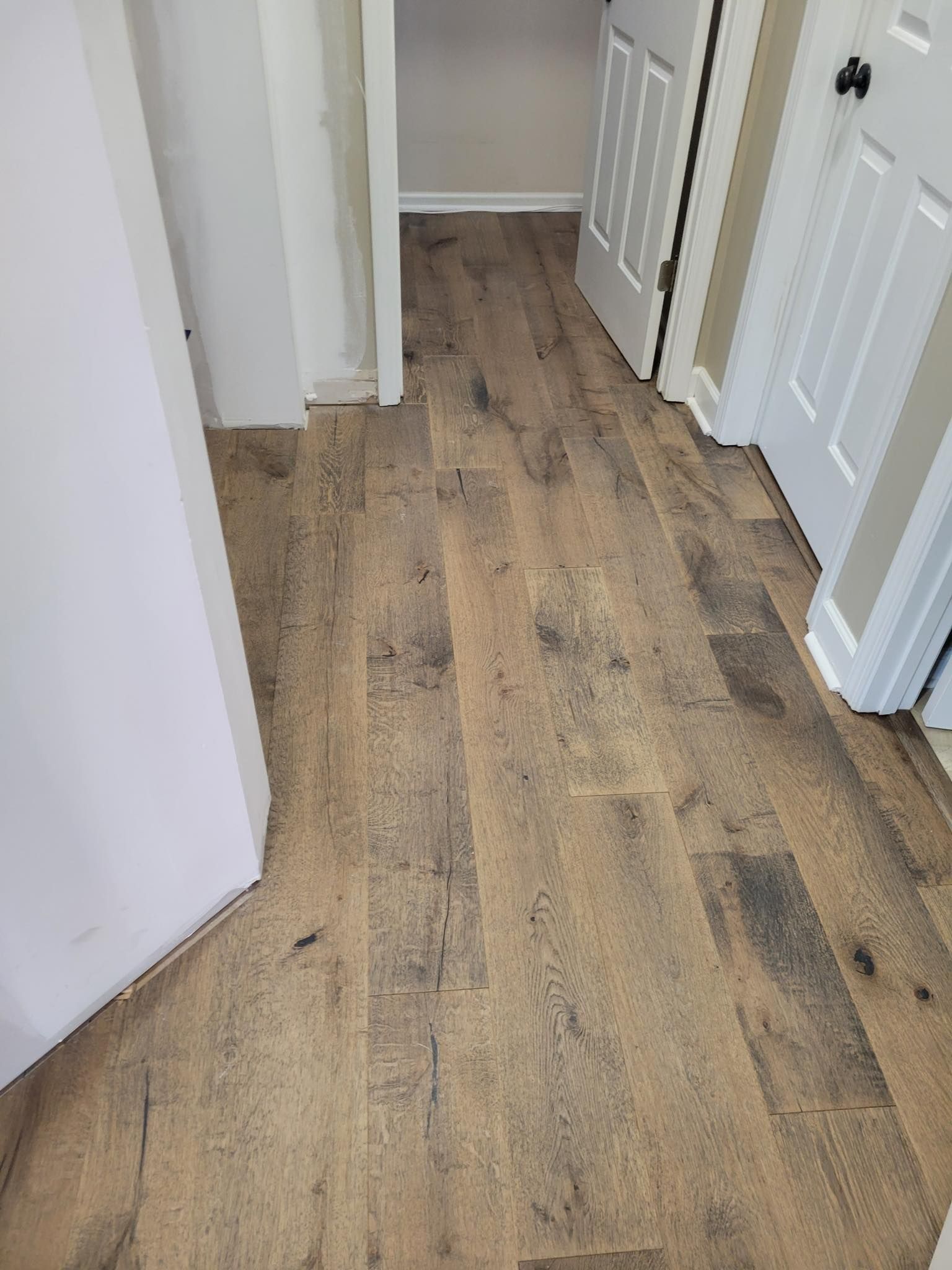 Wooden floor hallway with two white doors and a doorway.