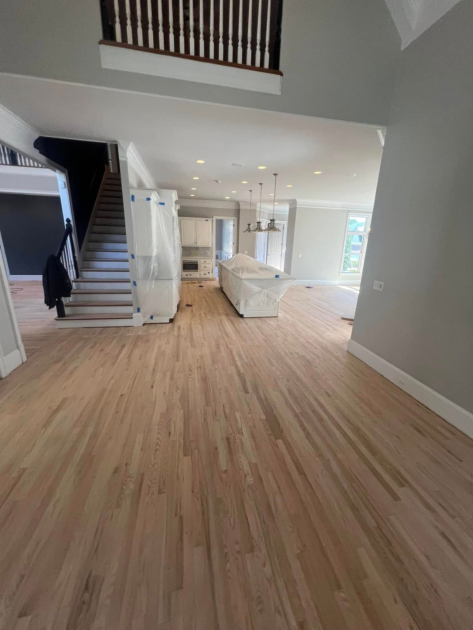 Spacious room with wood flooring, staircase, and kitchen island. White walls, grey accents.