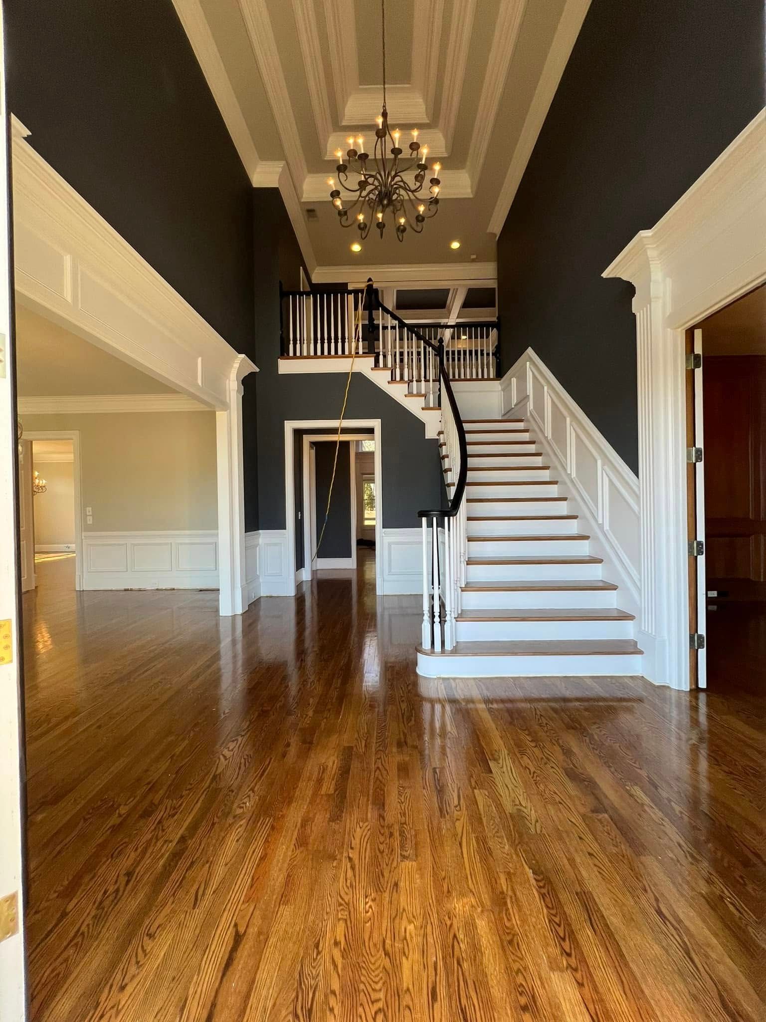 Grand entry hall with dark gray walls, white trim, staircase, chandelier, and hardwood floors.
