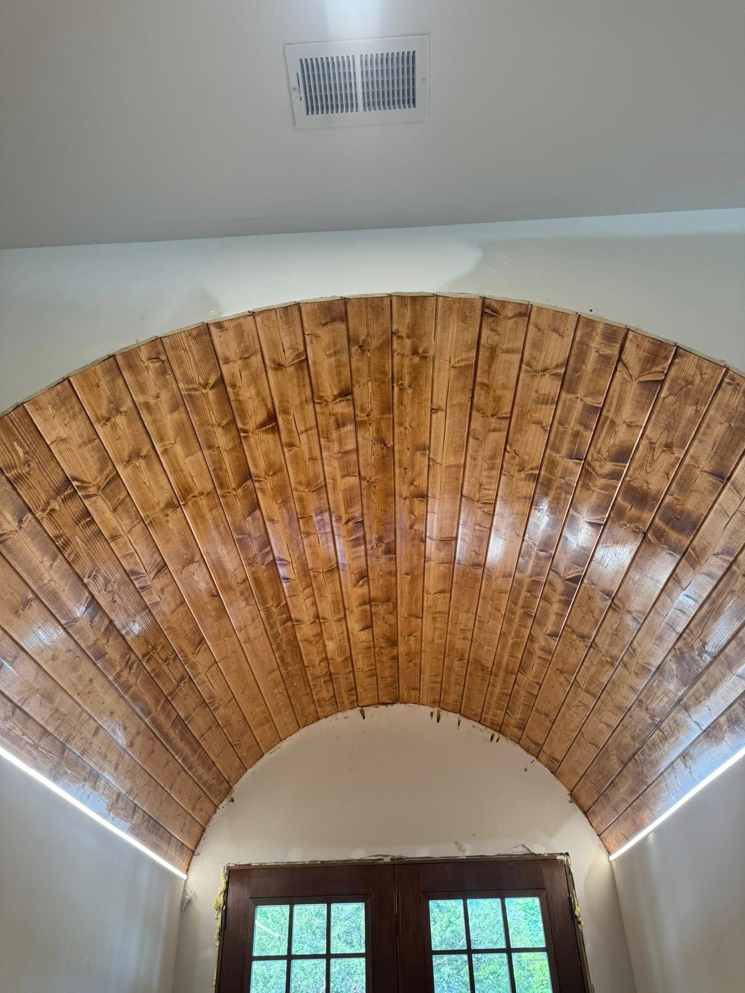 Wooden arched ceiling above a doorway, with recessed lighting and vent.