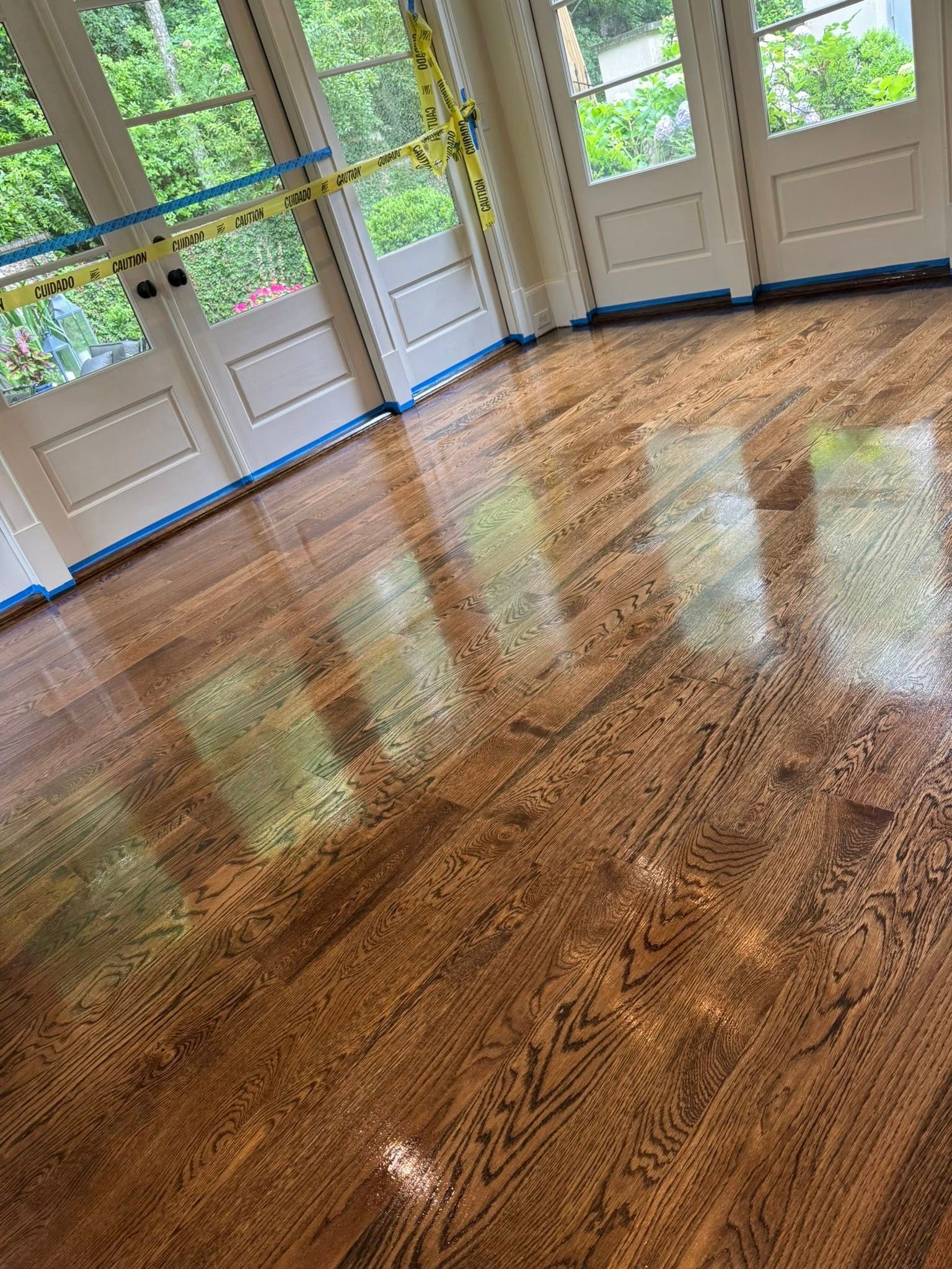 Newly finished, shiny hardwood floor reflecting light and windows. Doors along the wall.