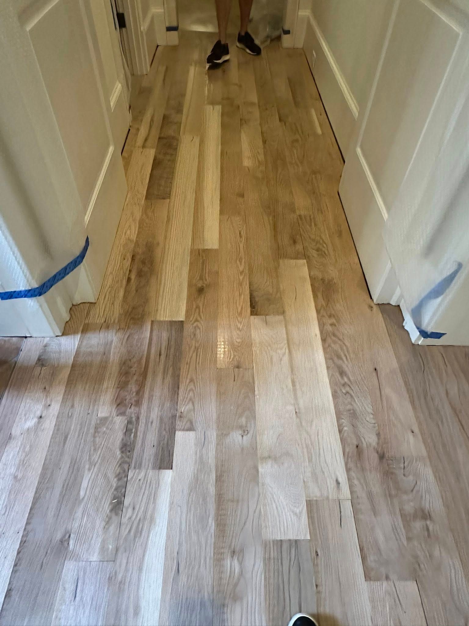 Hallway with light hardwood floors being installed. White trim and blue tape visible.