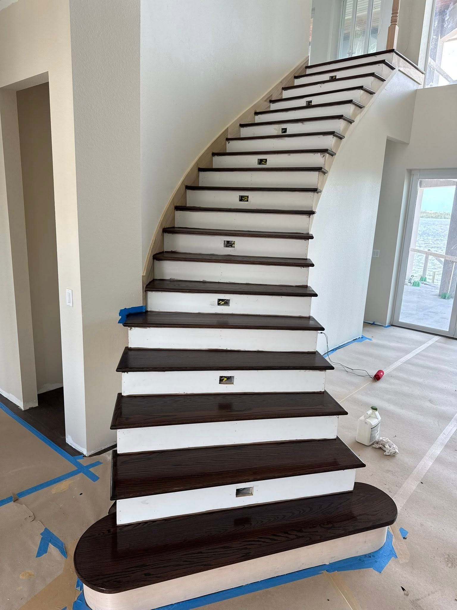 Curving staircase with dark wooden treads, white risers, and built-in lights, in a home under construction.