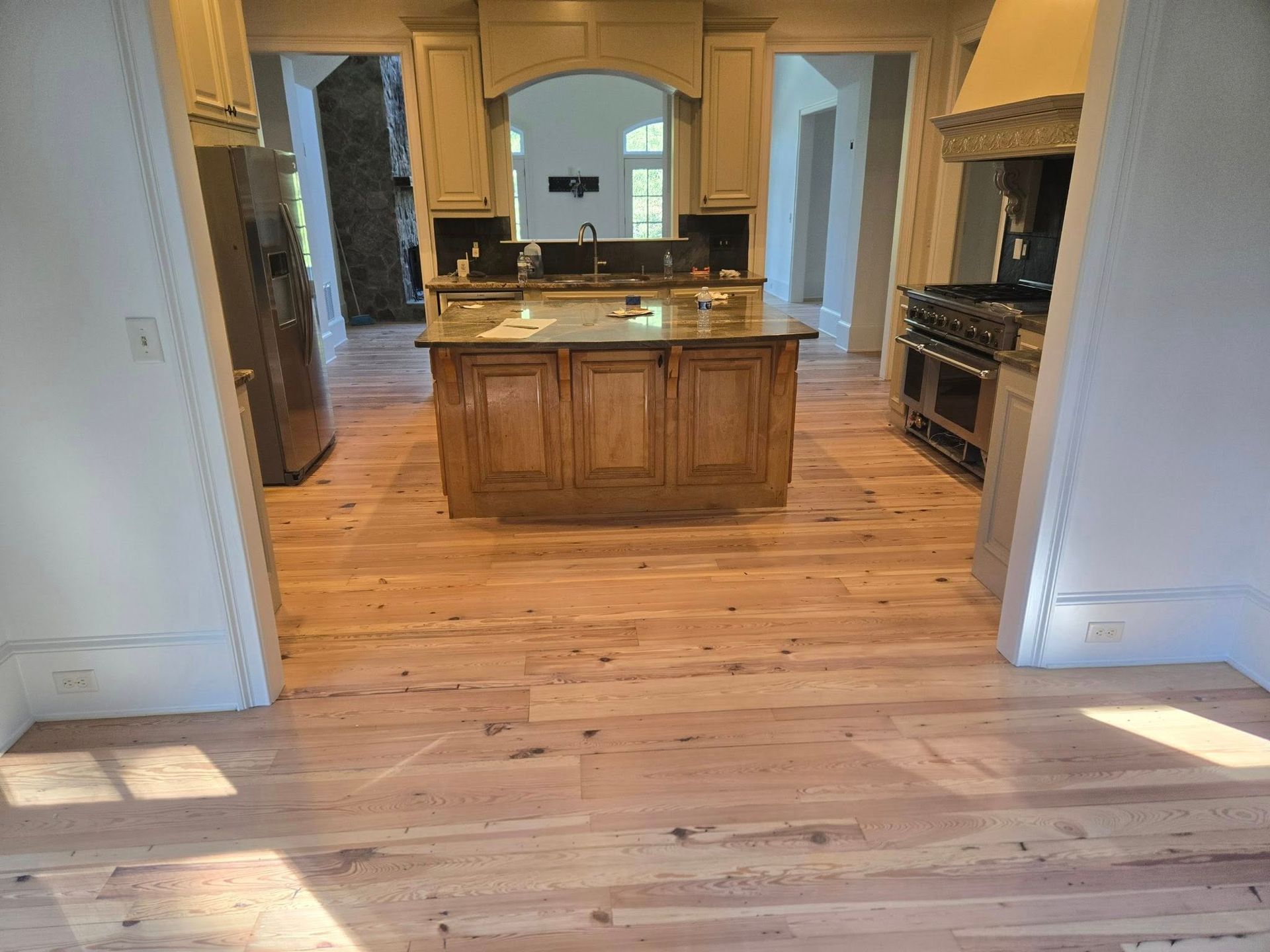 Light hardwood floor in a kitchen with a central island and a range with a hood.