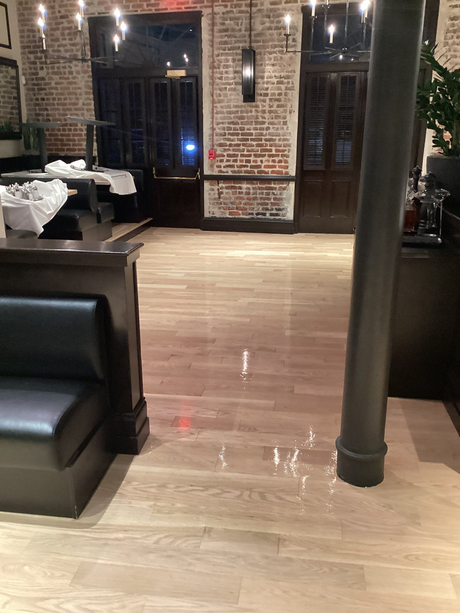 Restaurant interior with light wood flooring, brick walls, and a dark leather booth.