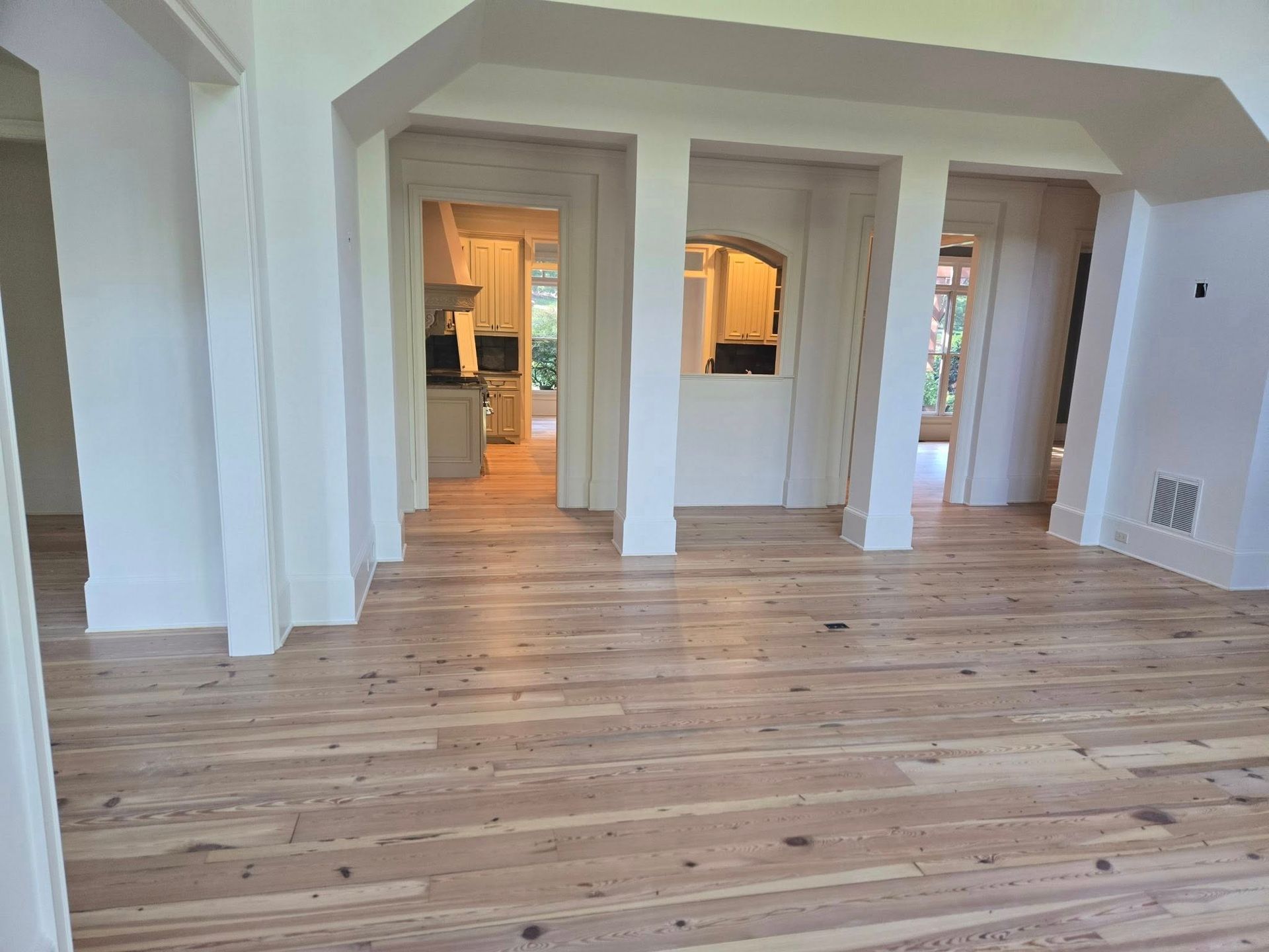 Hardwood floors in an open room with white pillars and doorways leading to other rooms.