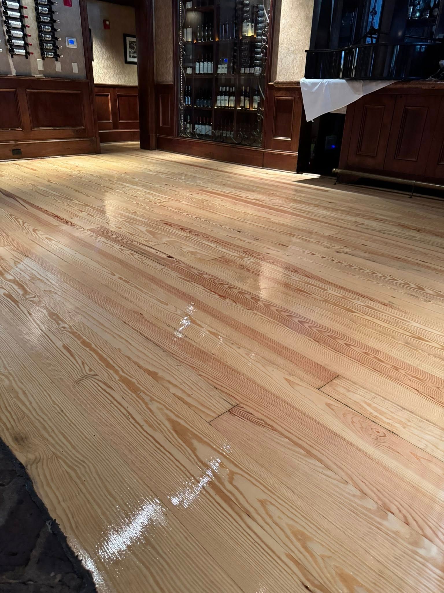 Wooden floor reflecting light in a restaurant with wine display in the background.