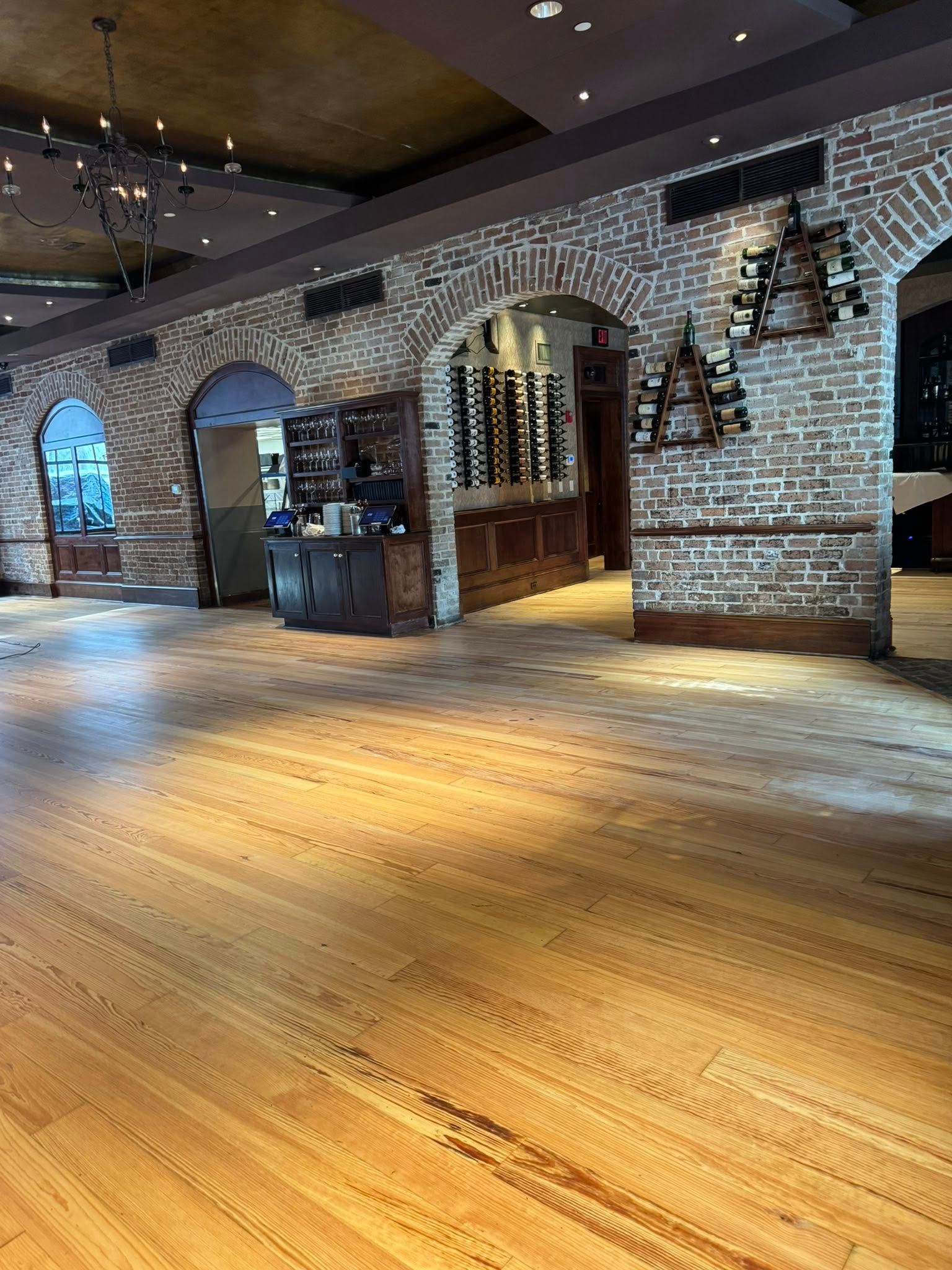 Empty restaurant interior with arched brick columns, wooden floor, and wine racks.
