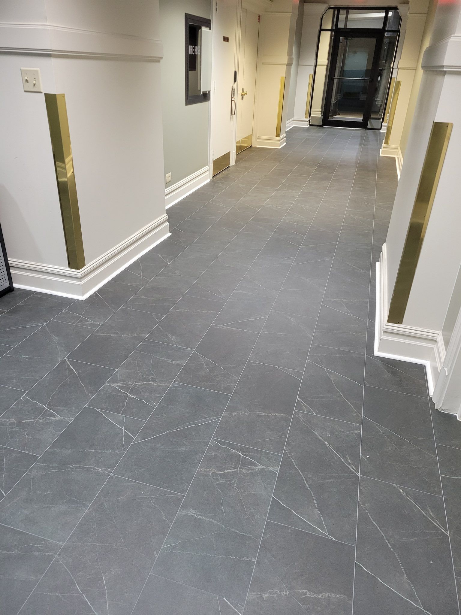 Long hallway with gray tile floor, white walls, and brass accents.