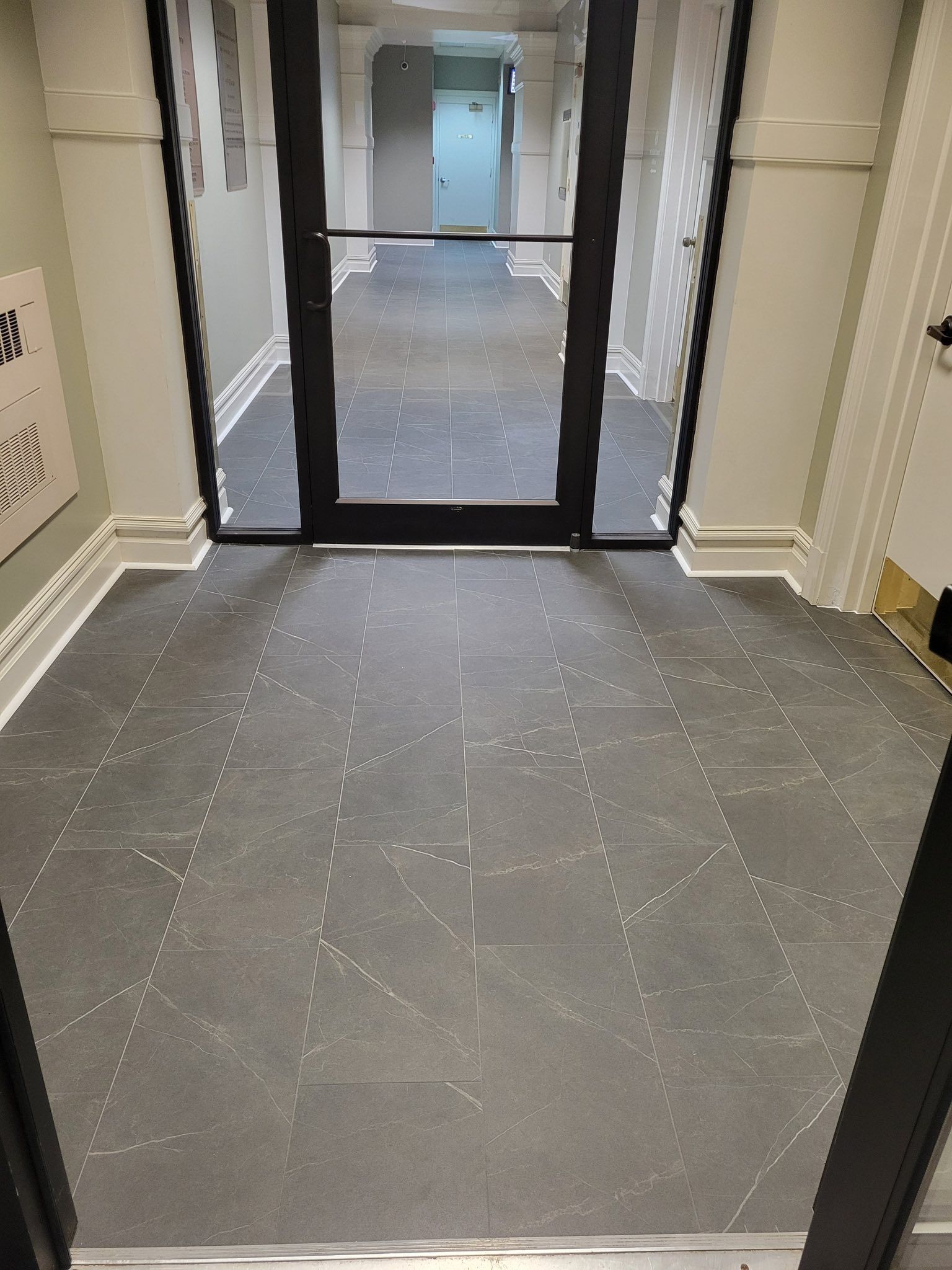 Hallway with dark tiled floor, glass door, and interior door at the end.
