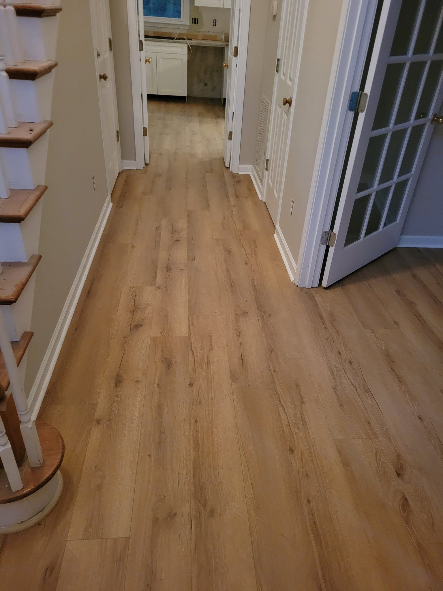 Hallway with wood-look flooring, leading to a kitchen. Staircase on the left, doors on both sides.