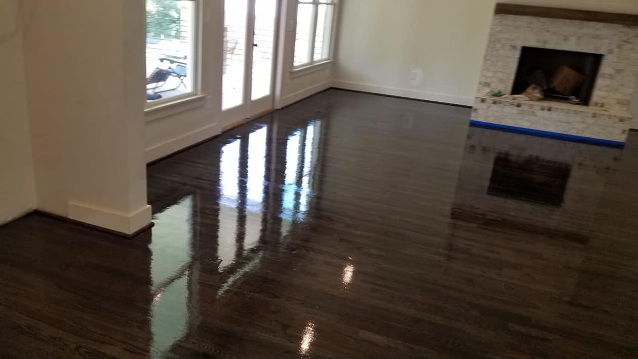 Dark stained hardwood floor with high gloss finish, reflecting windows and fireplace.
