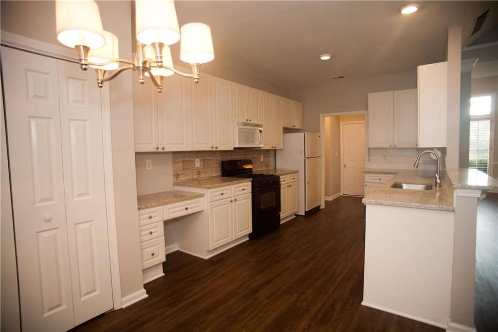 White kitchen with light cabinets, dark floor, and chandelier.