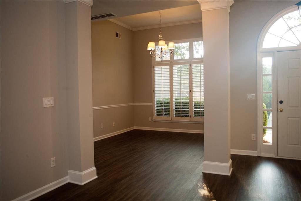 Empty dining room with dark wood floors, light gray walls, and chandelier.
