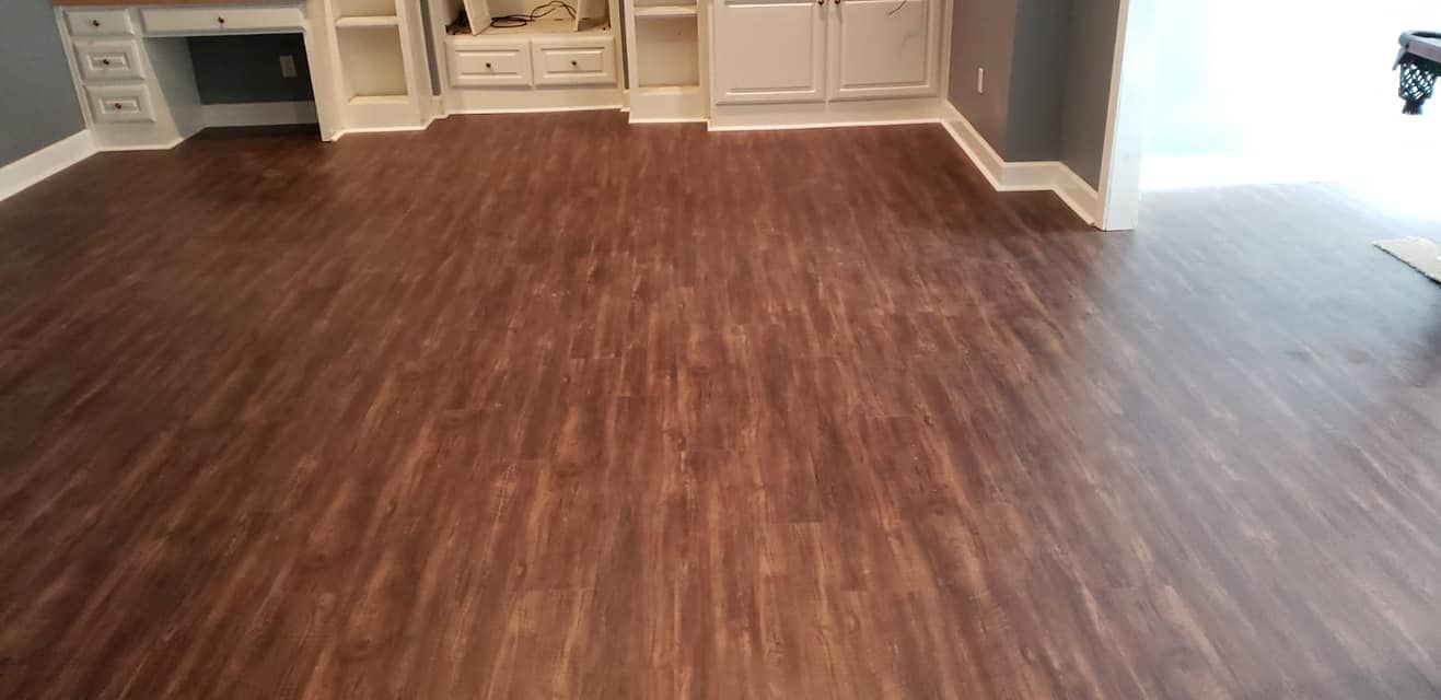 Brown wooden floor in a room with white cabinets and a gray wall.
